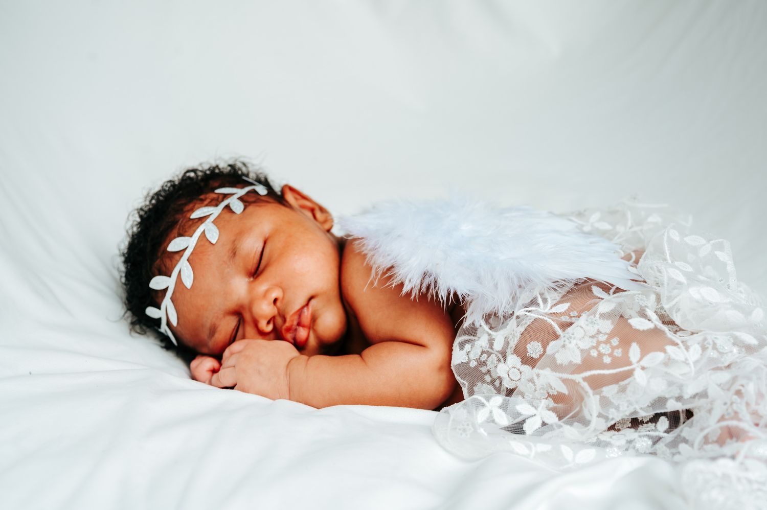 Sleeping newborn baby in white lace wrap against light background.