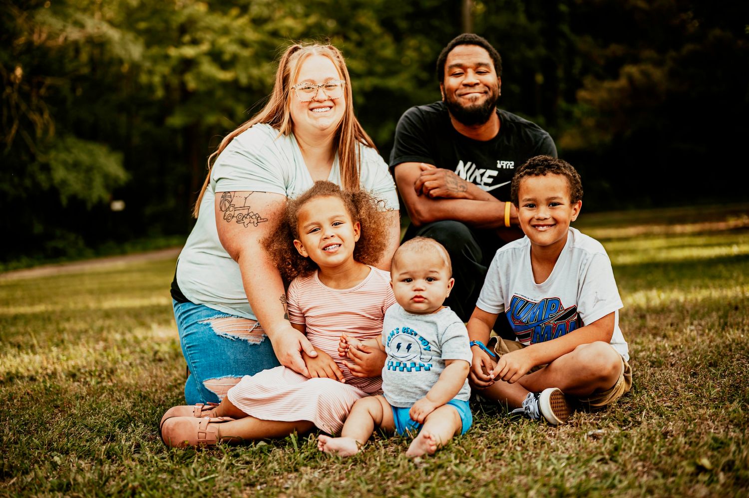 Family enjoying a playful moment together on grass during golden hour outdoor photo session.