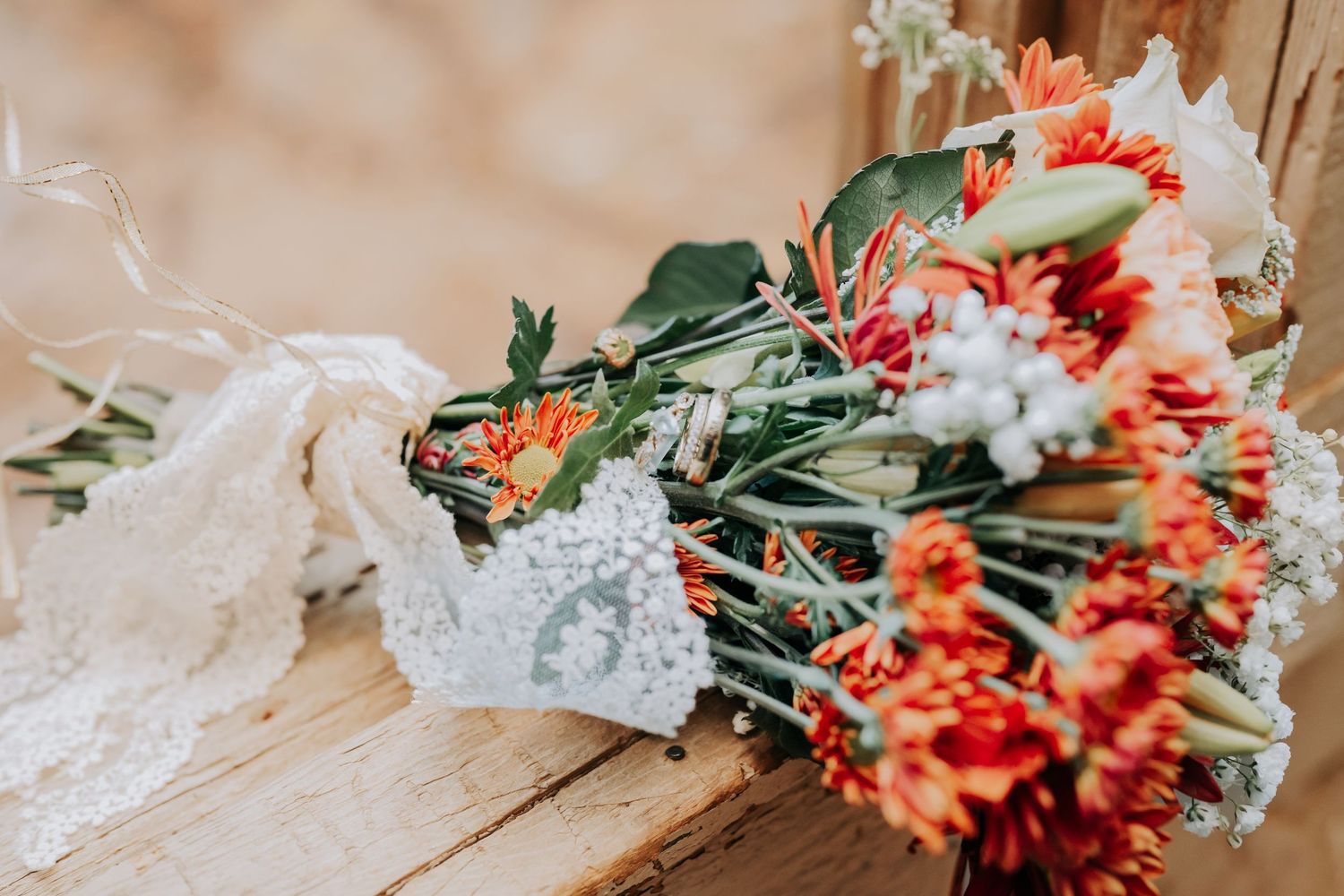 Delicate lace wedding bouquet with orange and white flowers against rustic wooden background.