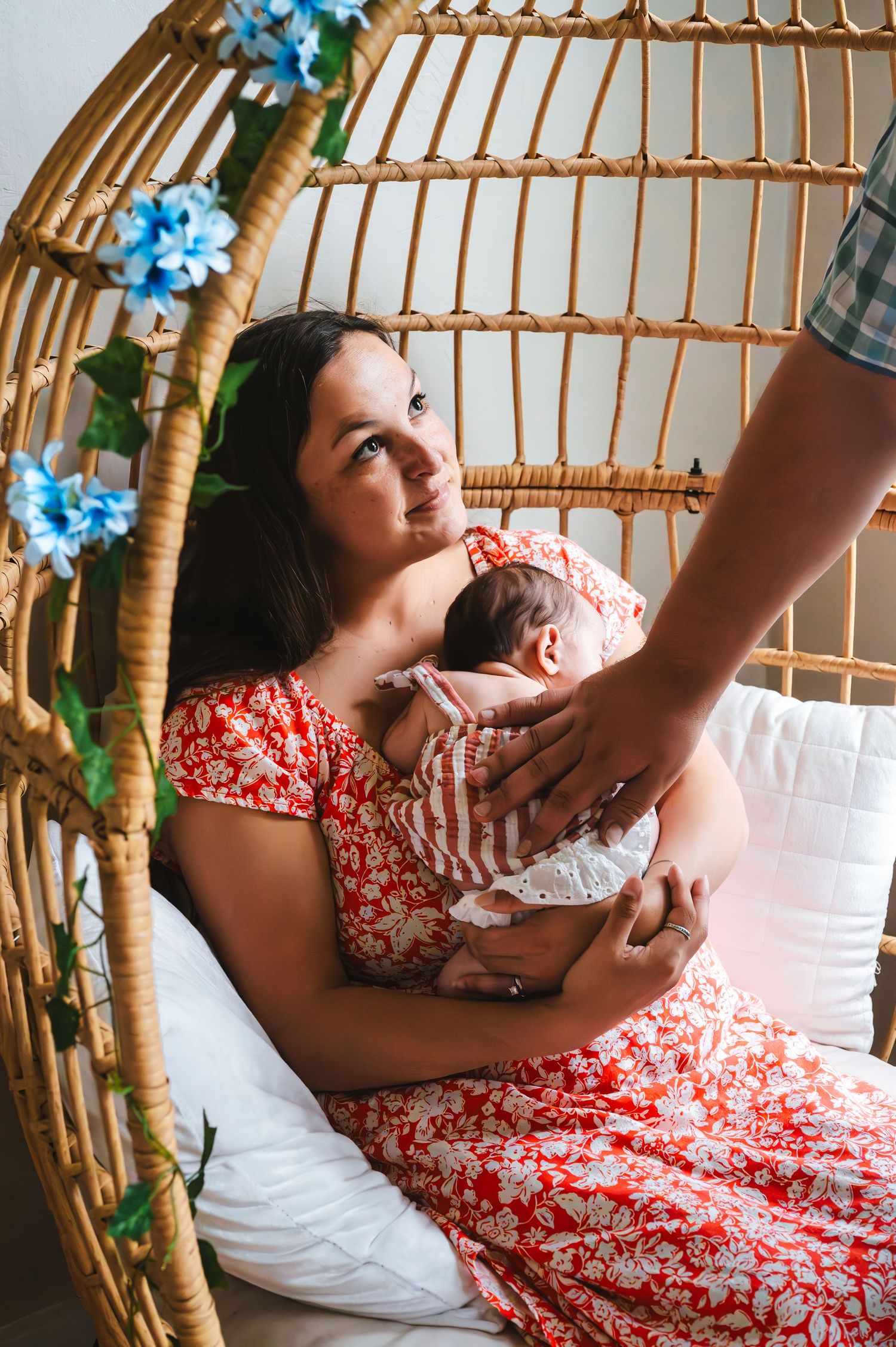 Mother and newborn rest in wicker chair decorated with blue flowers.