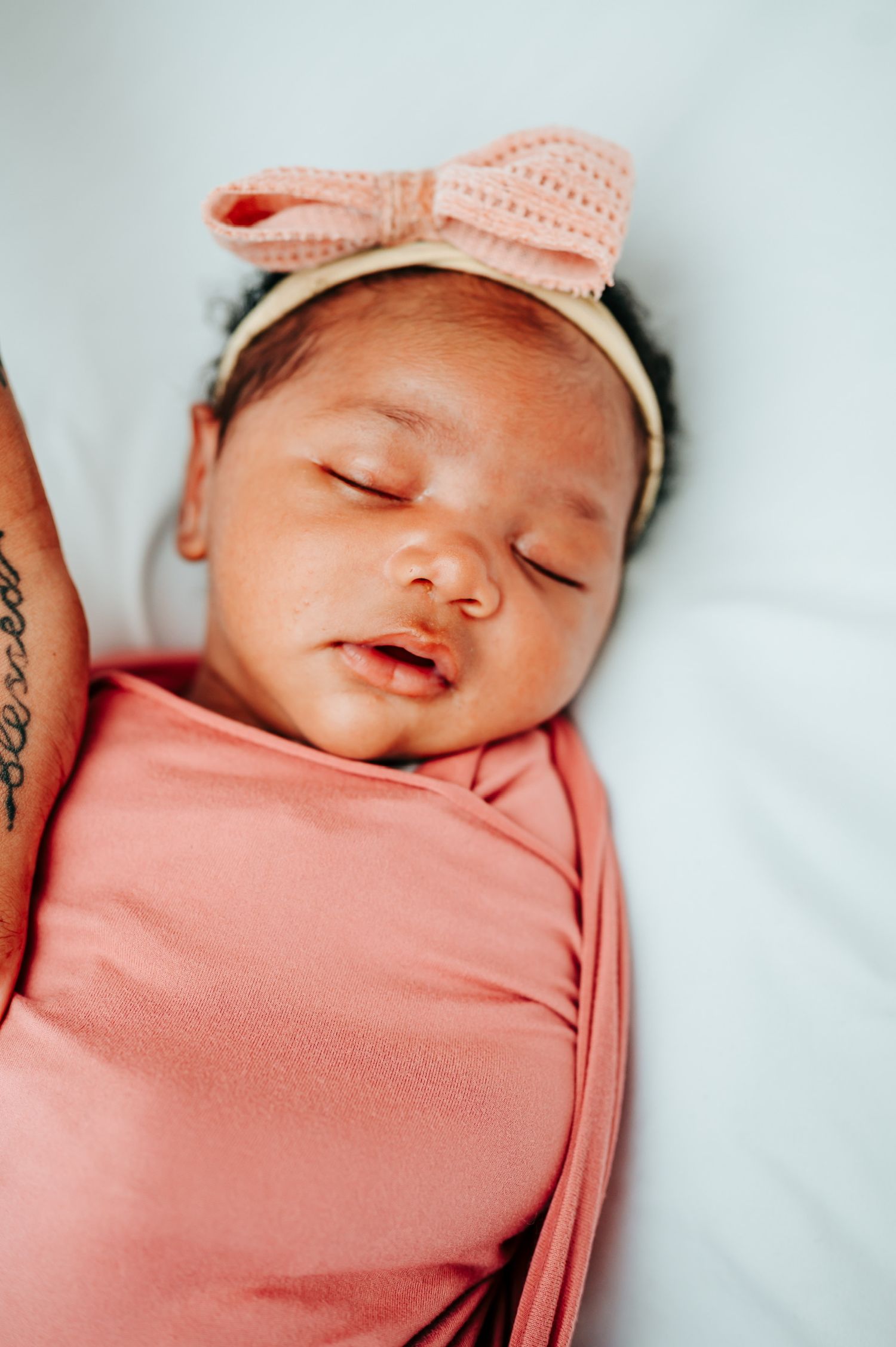 Sleeping newborn baby wrapped in soft pink swaddle wearing knit hat.