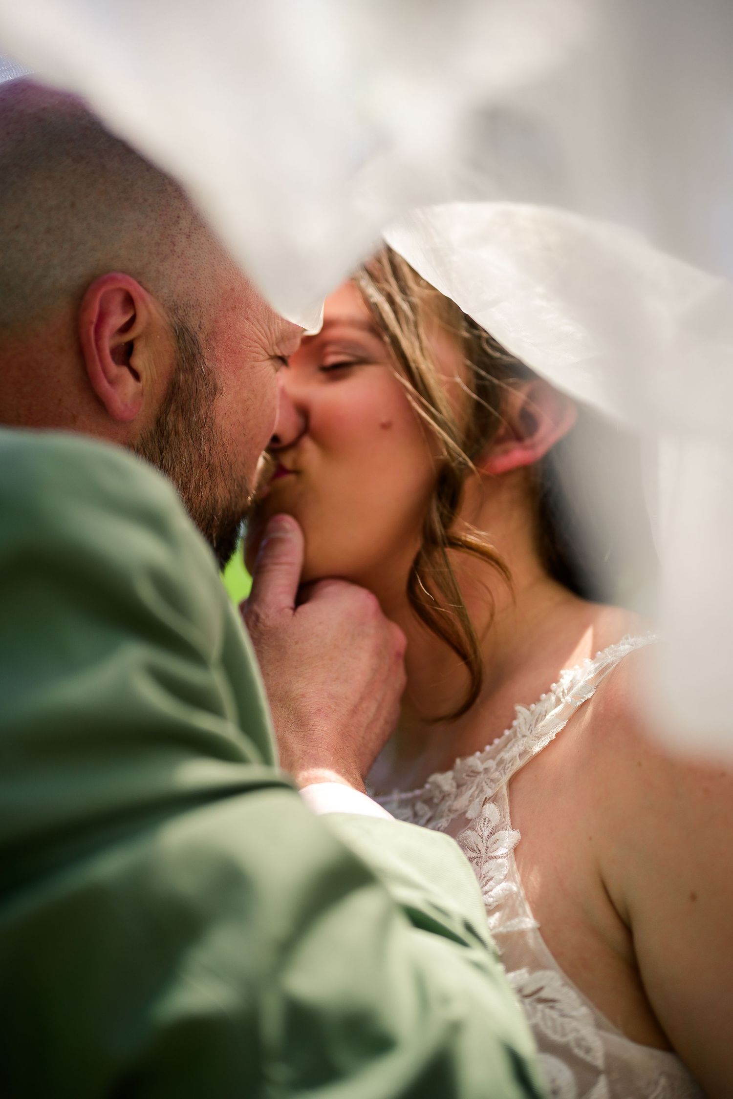 Bride and groom sharing romantic kiss under wedding veil on their special day.