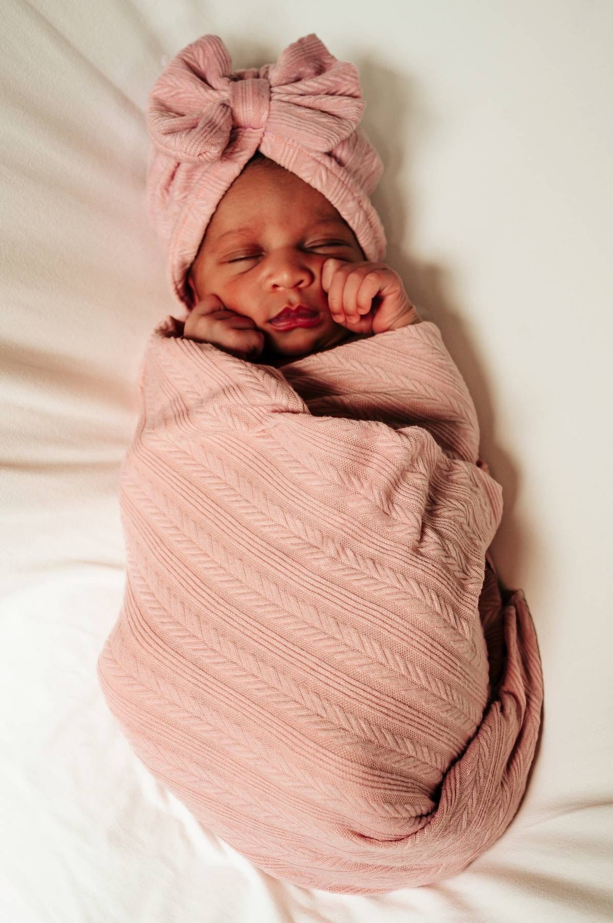 Newborn baby wrapped in soft pink swaddle blanket during professional photo session.