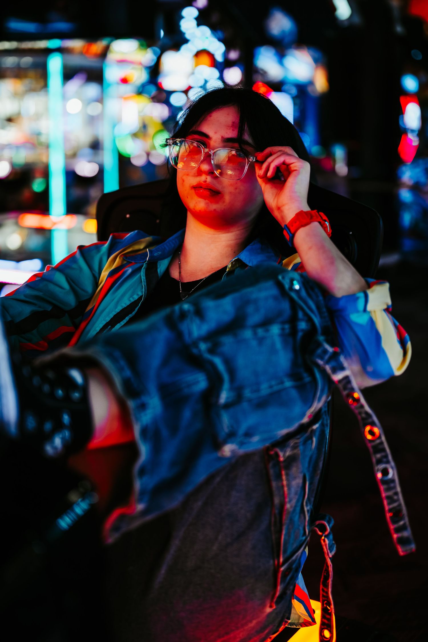 Young woman adjusting glasses under colorful neon lights at night in urban setting.