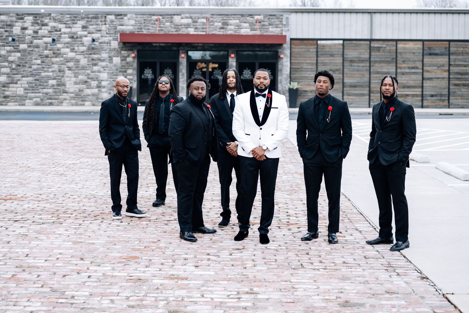 A group of people in formal black attire walk together in the snow outside a stone building.