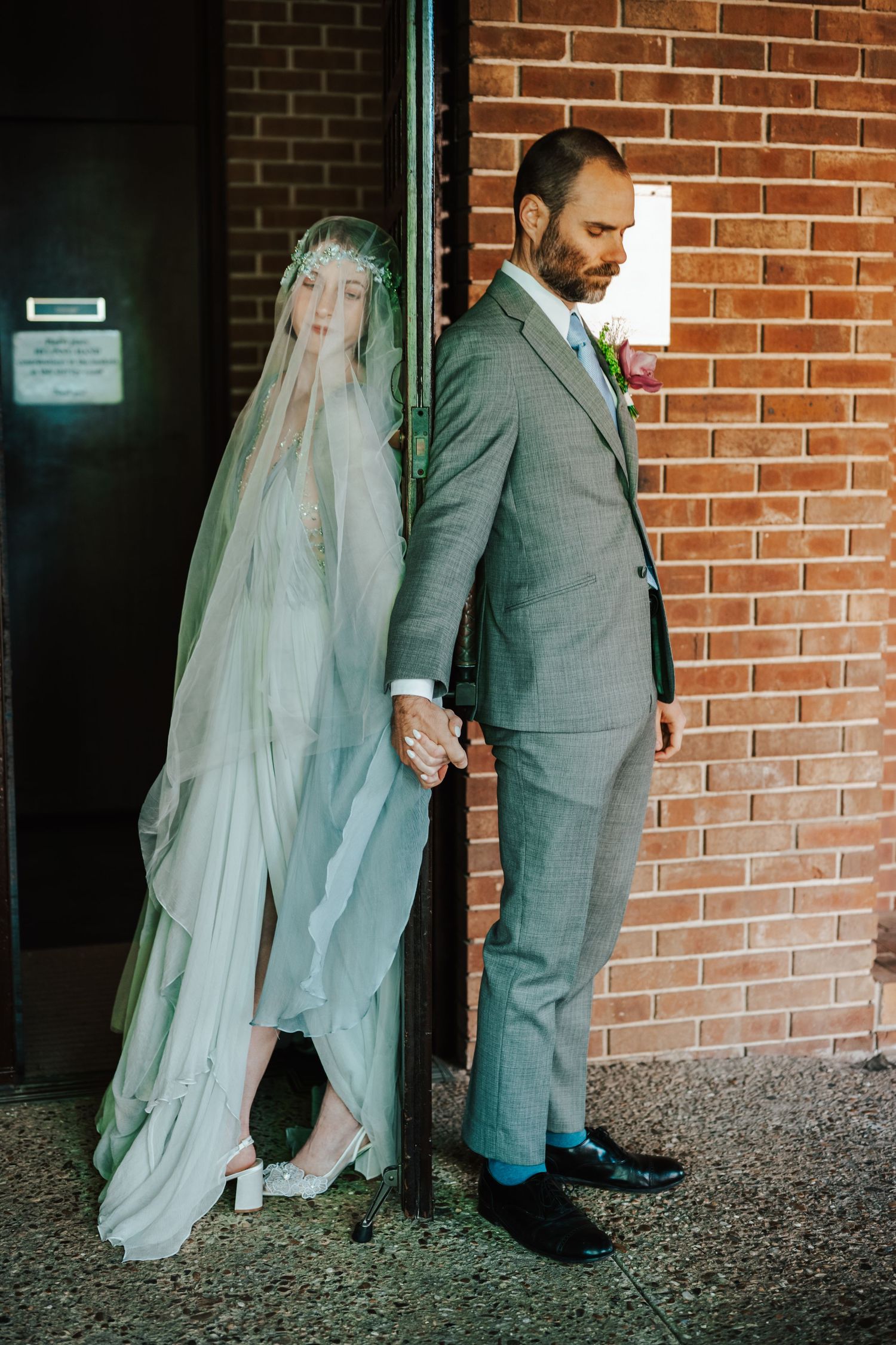 A bride and groom share a private prayer against a brick wall before their wedding ceremony.
