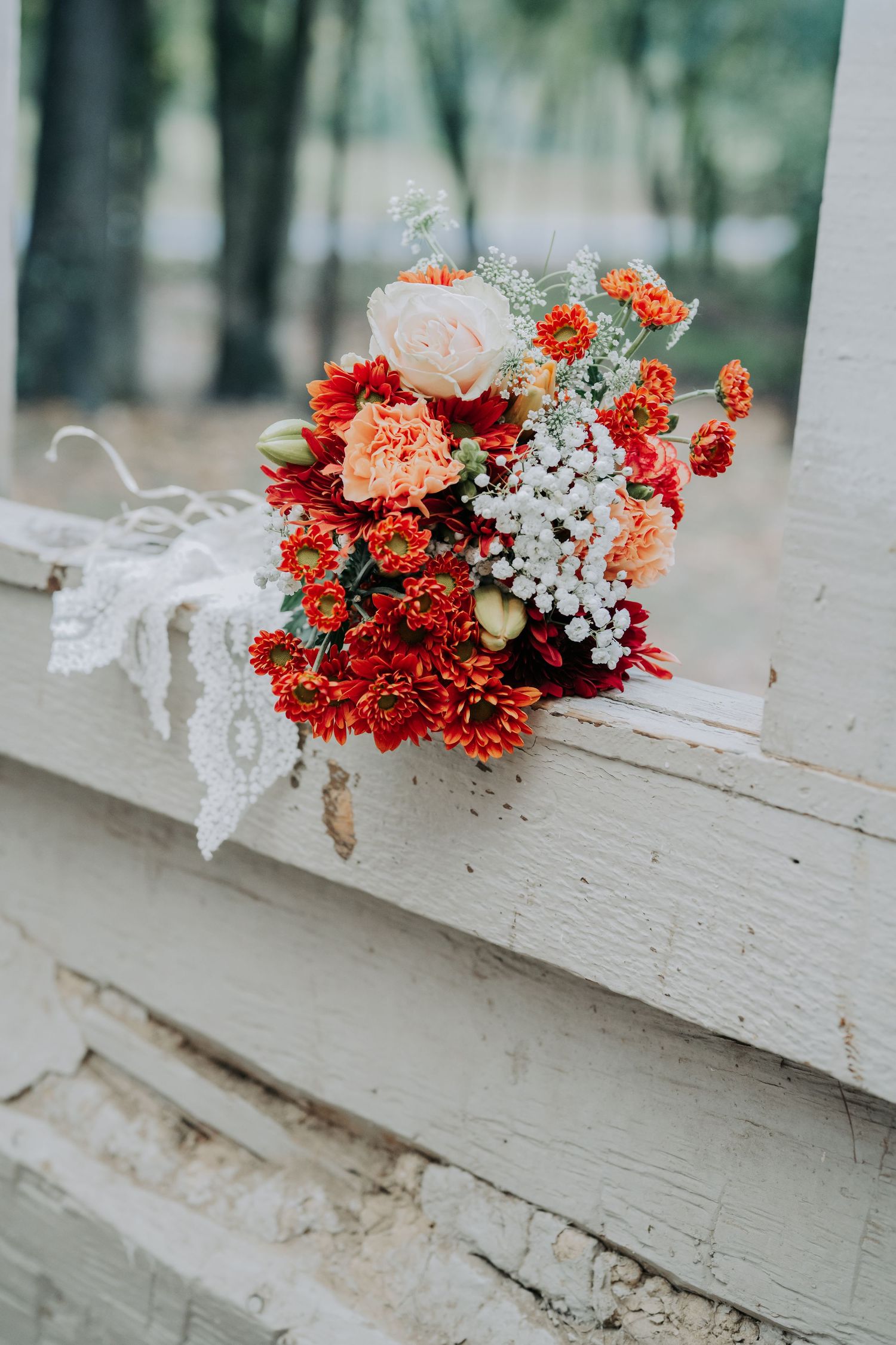 Red and peach carnations with baby's breath arranged on a white wooden fence.