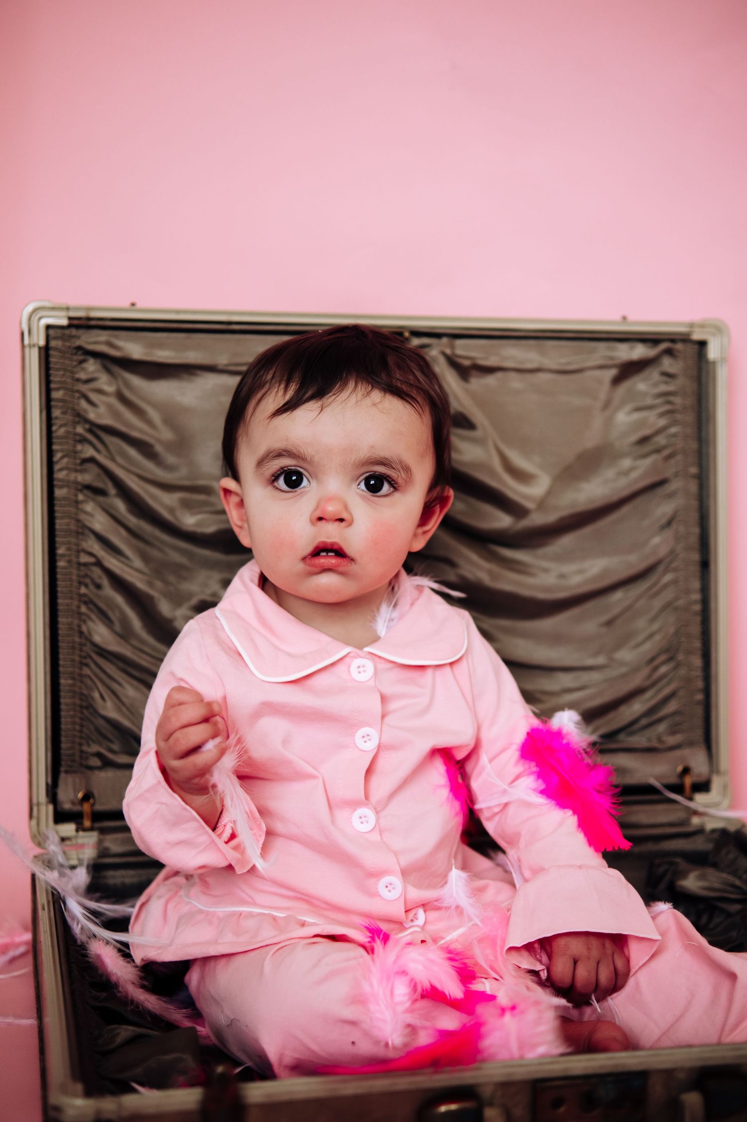 Baby wearing pink dress and tutu sits on brown backdrop in series of studio portraits.