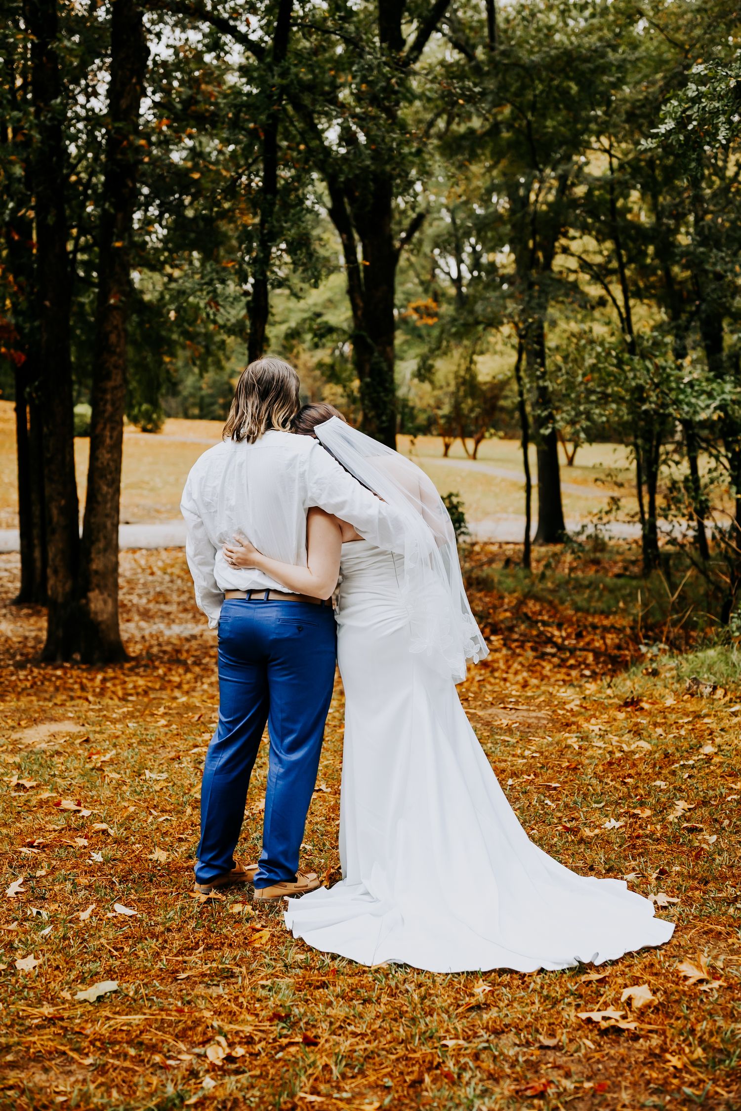 Wedding couple walking together through fallen autumn leaves in wooded area.