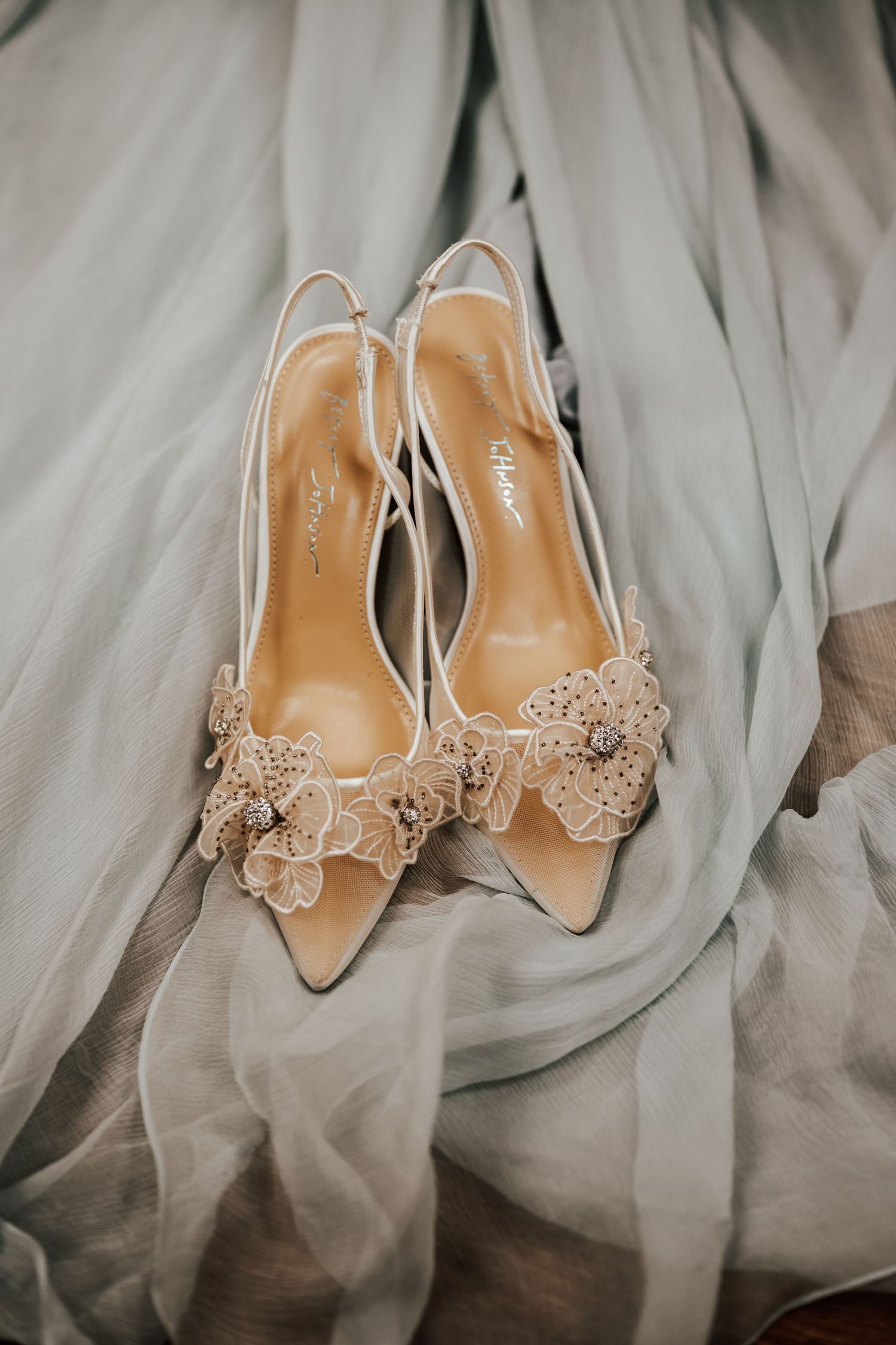 Elegant beige bridal shoes with delicate butterfly embellishments rest against soft tulle fabric.