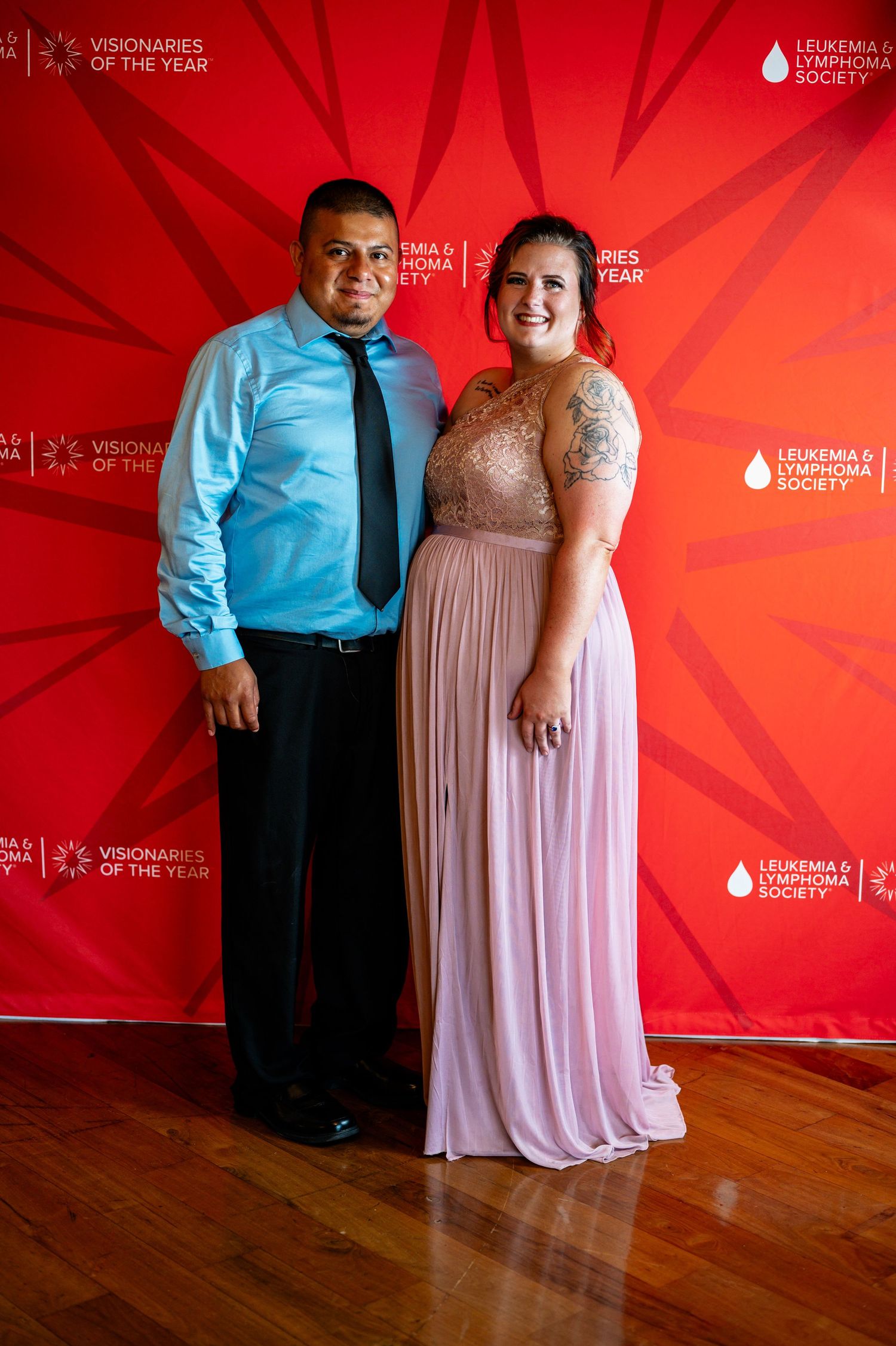 Couple in formal attire posing against red backdrop at special event.