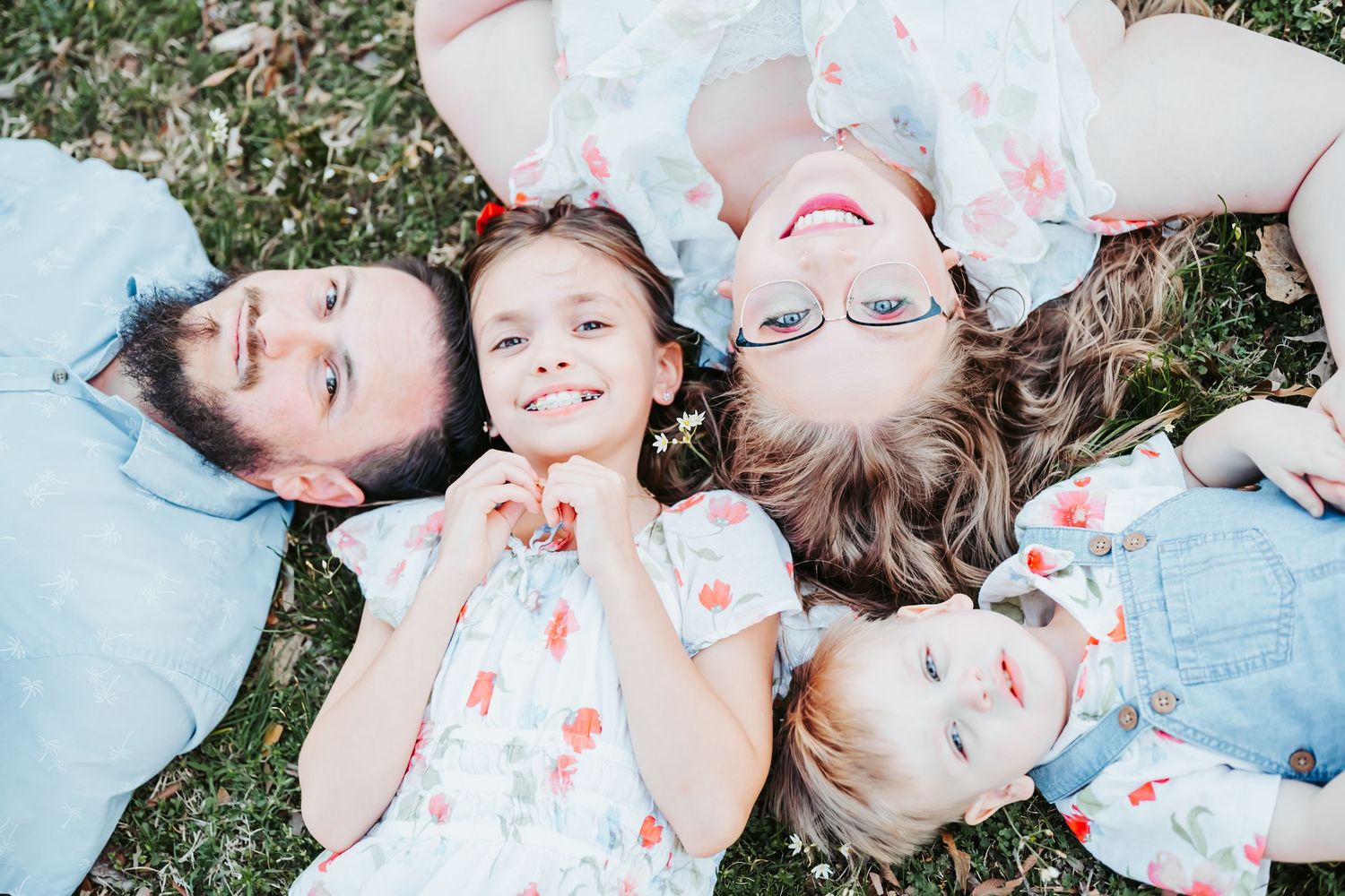Aerial view of happy family with two young daughters lying on green grass smiling up at camera.