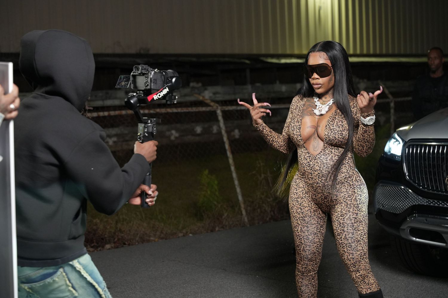 Woman in leopard print catsuit posing for camera crew outdoors at night.