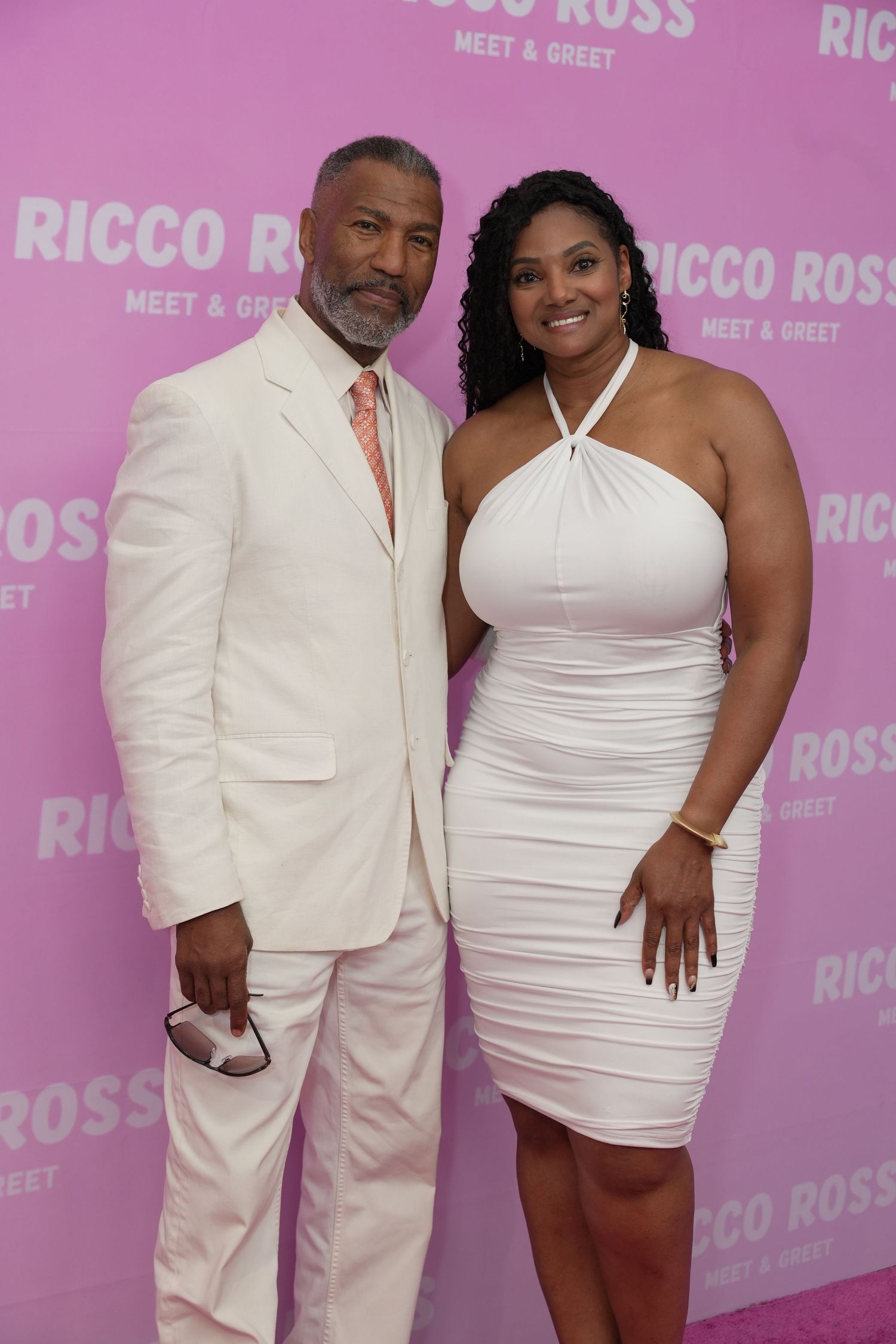 Man in white suit and woman in white dress posing at Ricco Ross Meet and Greet event.