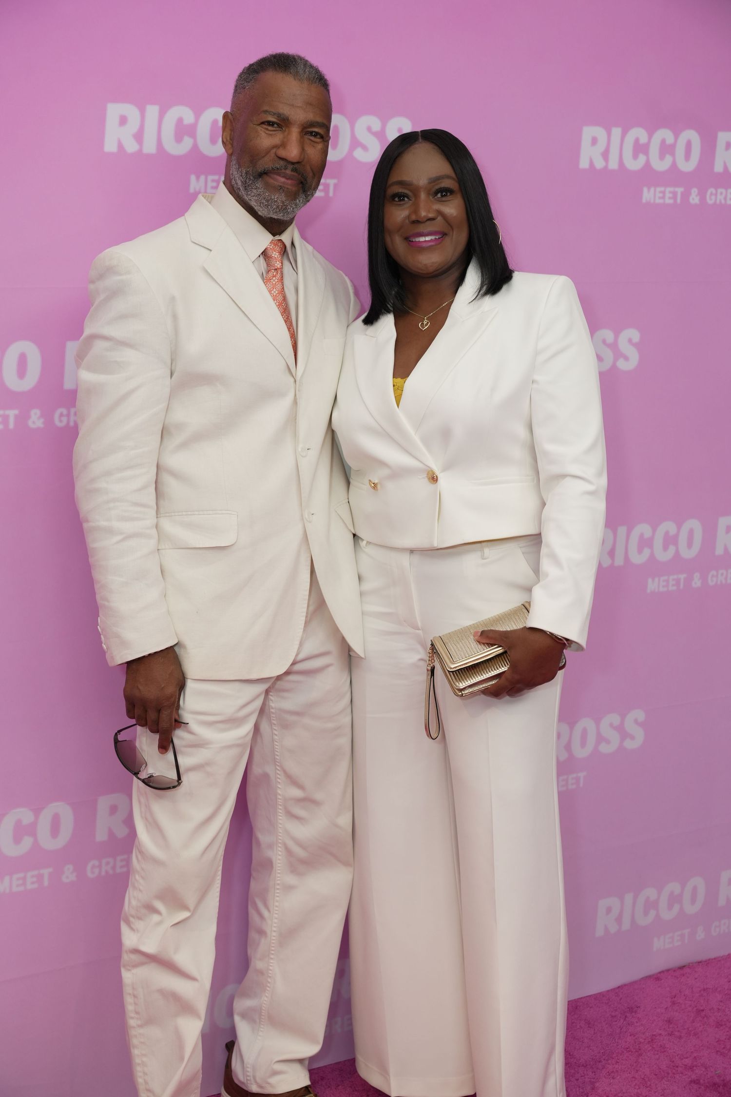 Fan posing with Ricco Ross at the mother's day Meet & Greet event, wearing elegant white outfits against a pink branded backdrop.