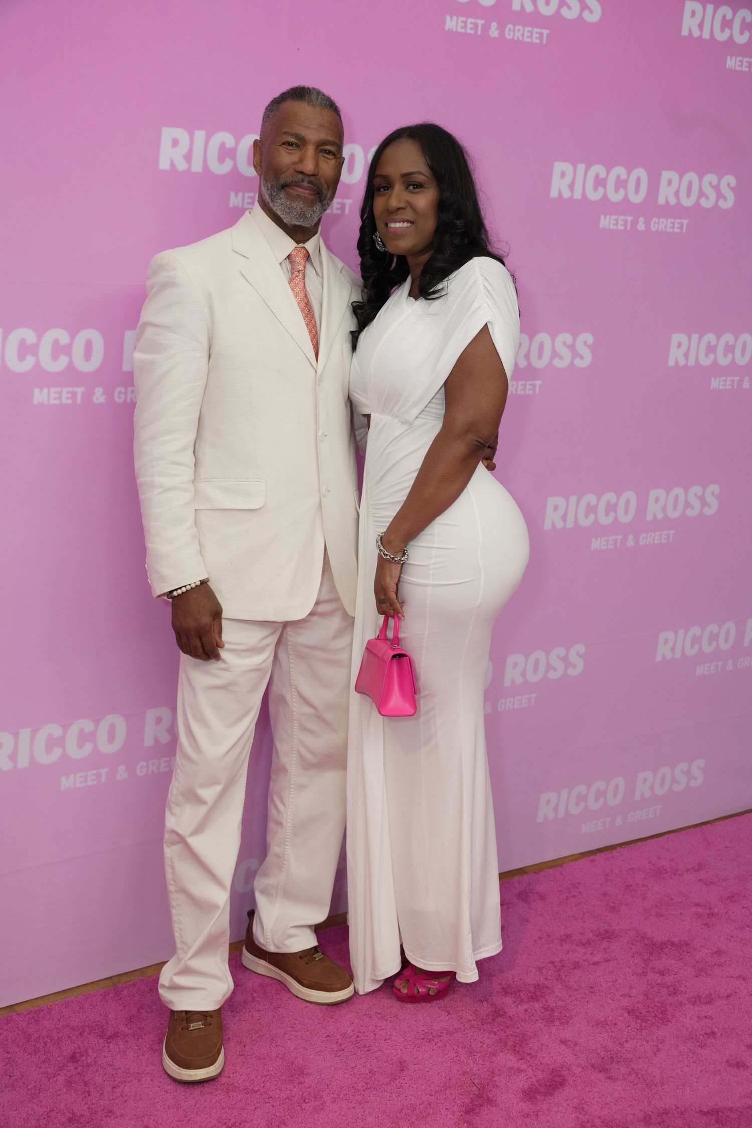 Fan posing with Ricco Ross at the mother's day Meet & Greet event, wearing elegant white outfits against a pink branded backdrop.