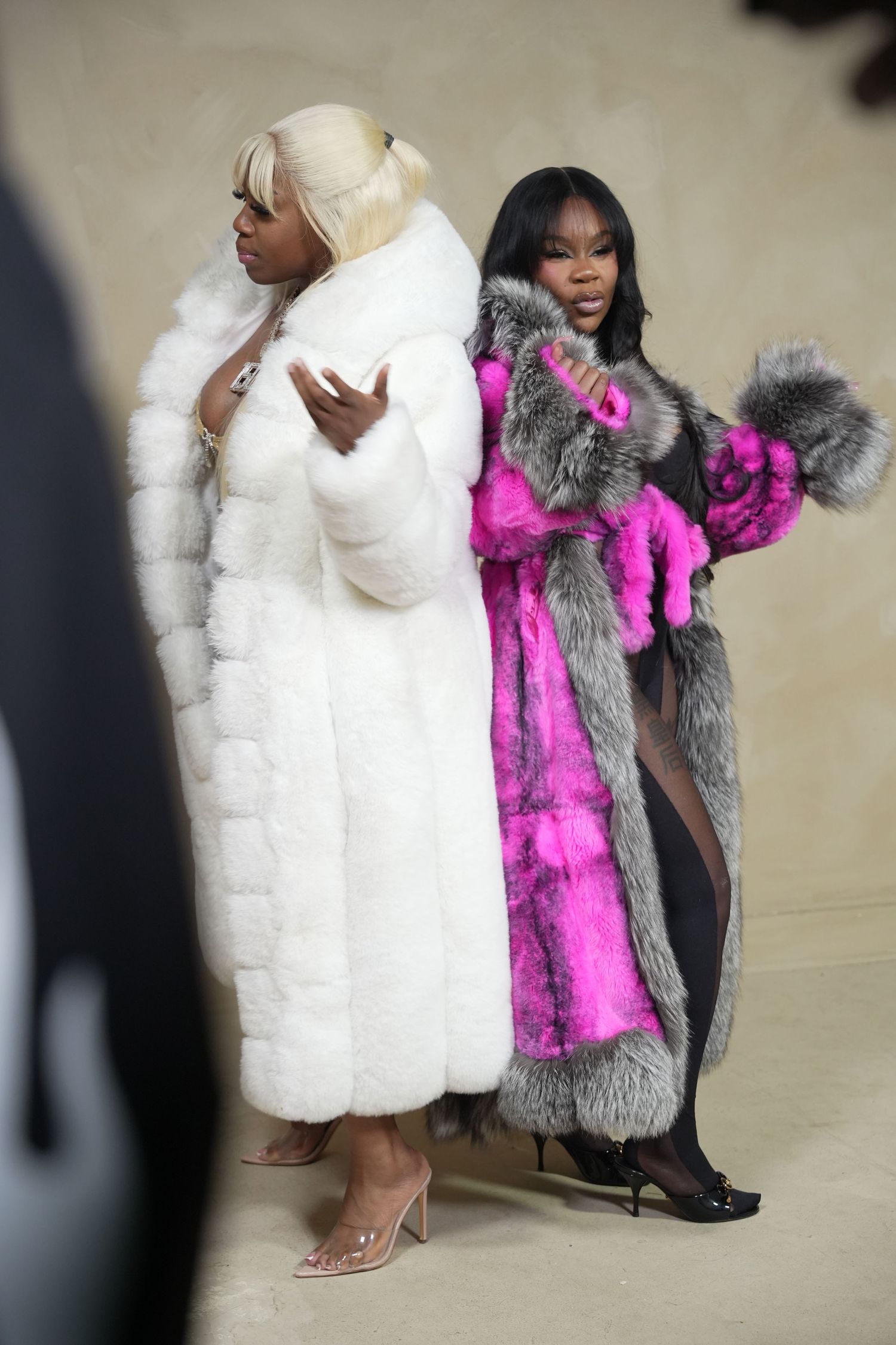 Two women wearing luxury fur coats, one white and one pink with gray fur trim.