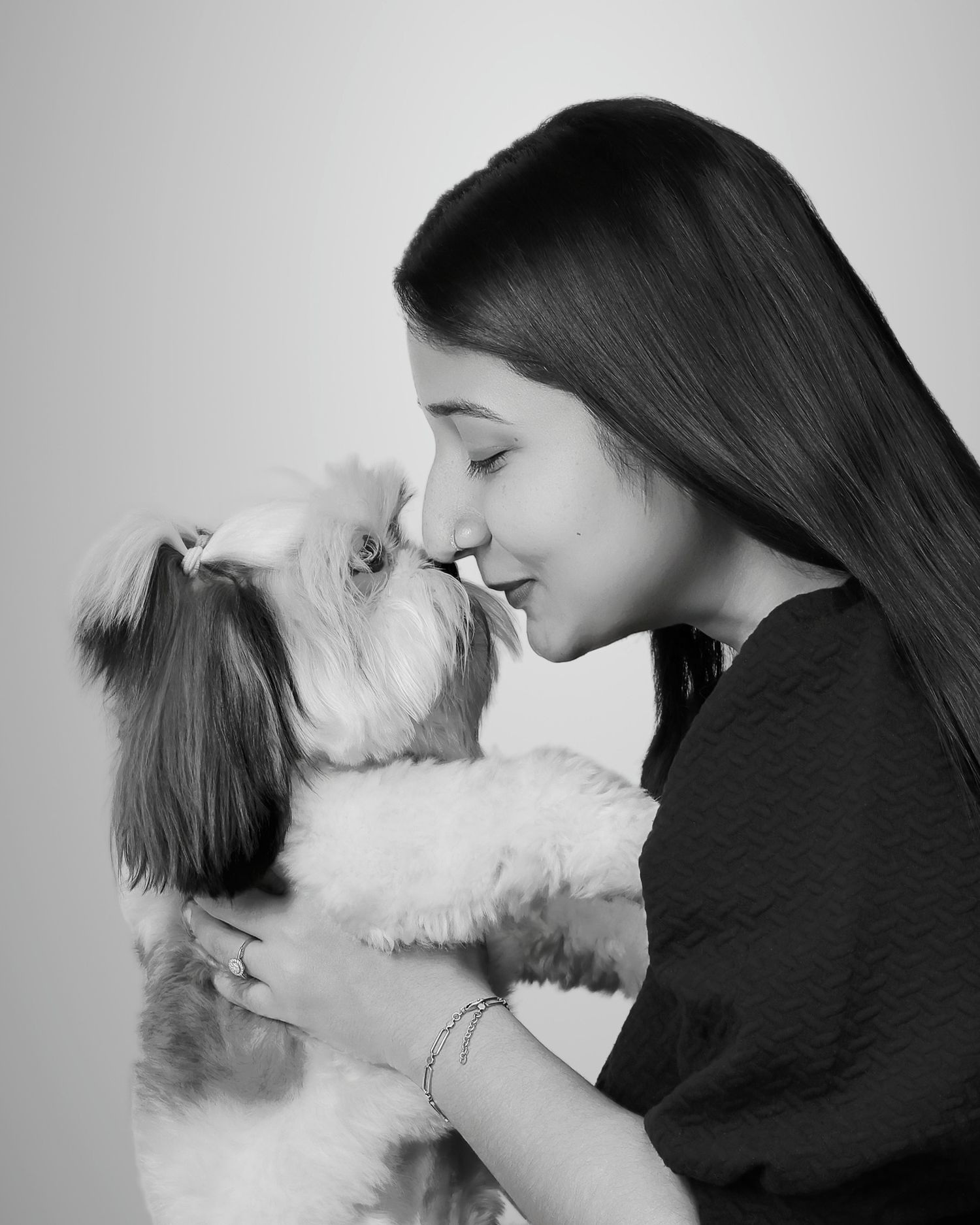 Black and white photo of a young woman with long hair affectionately touching noses with a fluffy Shih Tzu dog.