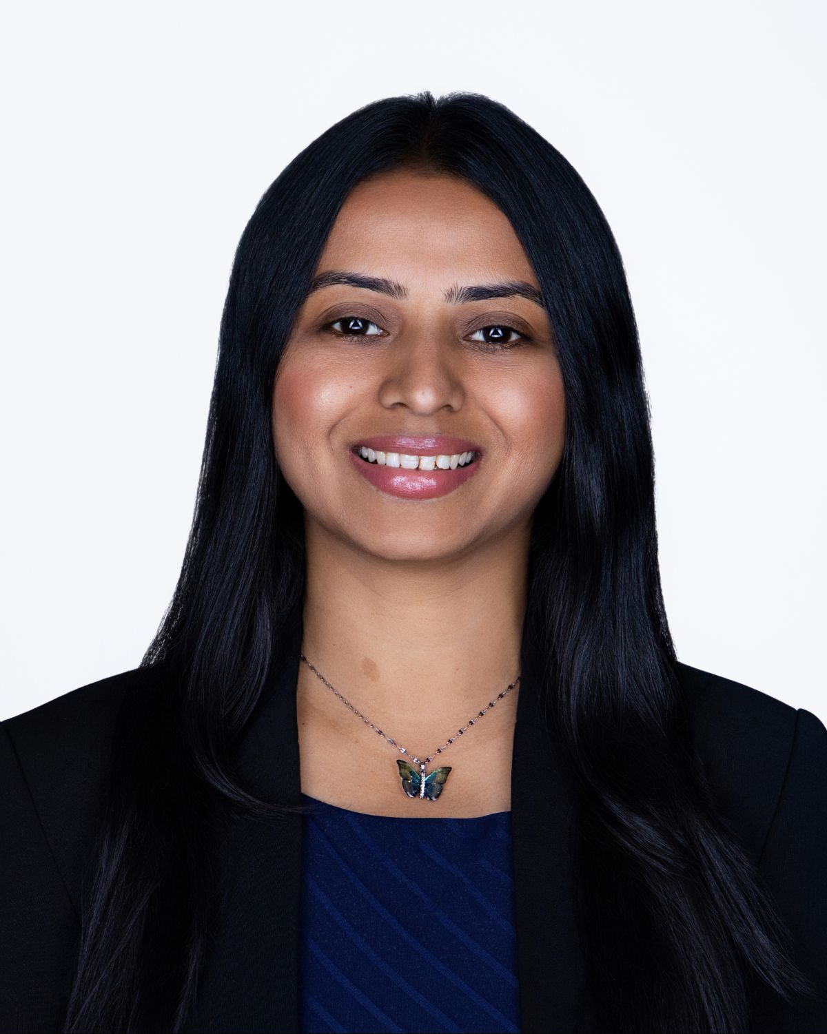 Professional headshot of a smiling woman with long black hair wearing a black blazer and butterfly necklace.