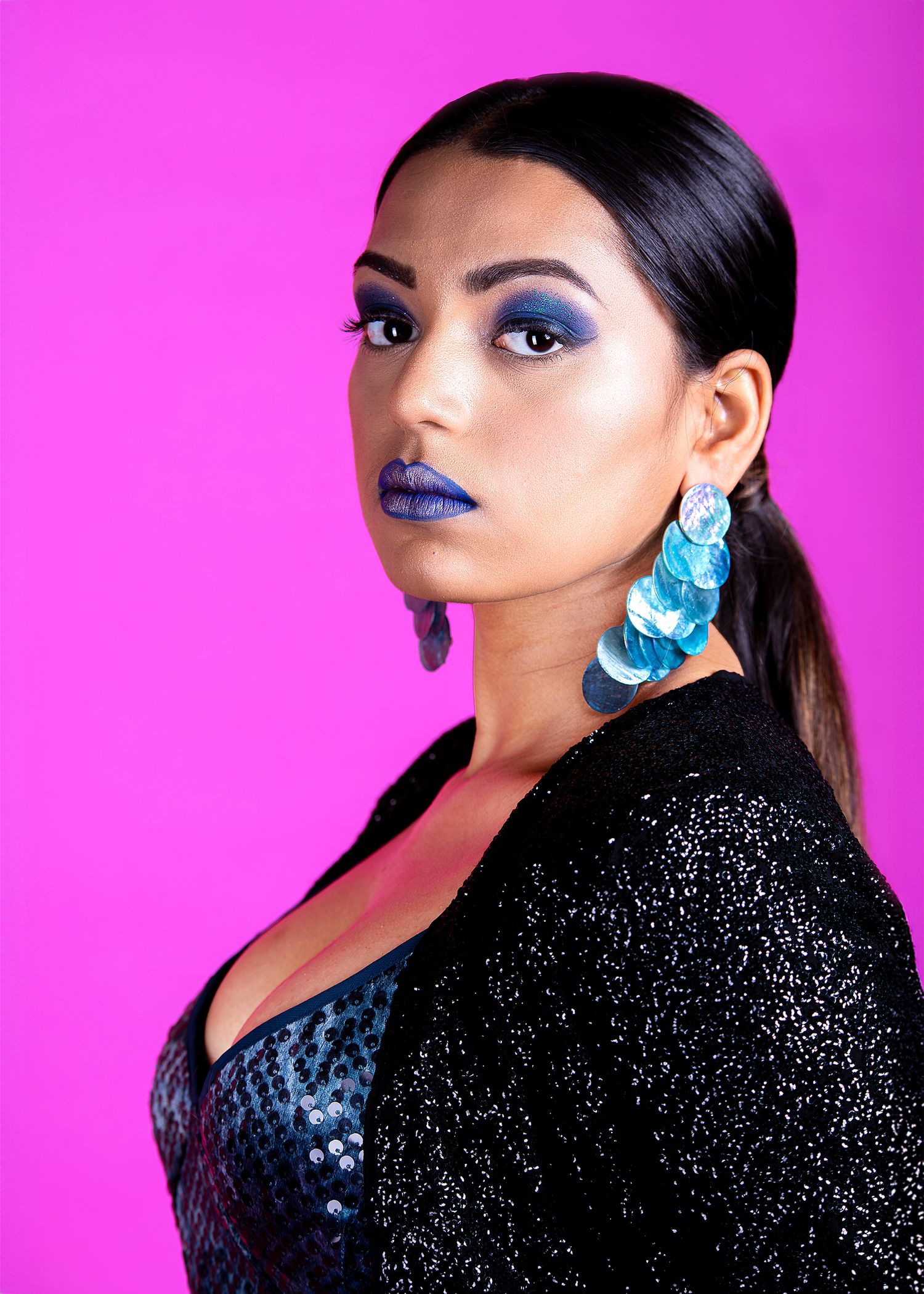 Glamour portraits with blue earrings and sparkly black dress against pink background.