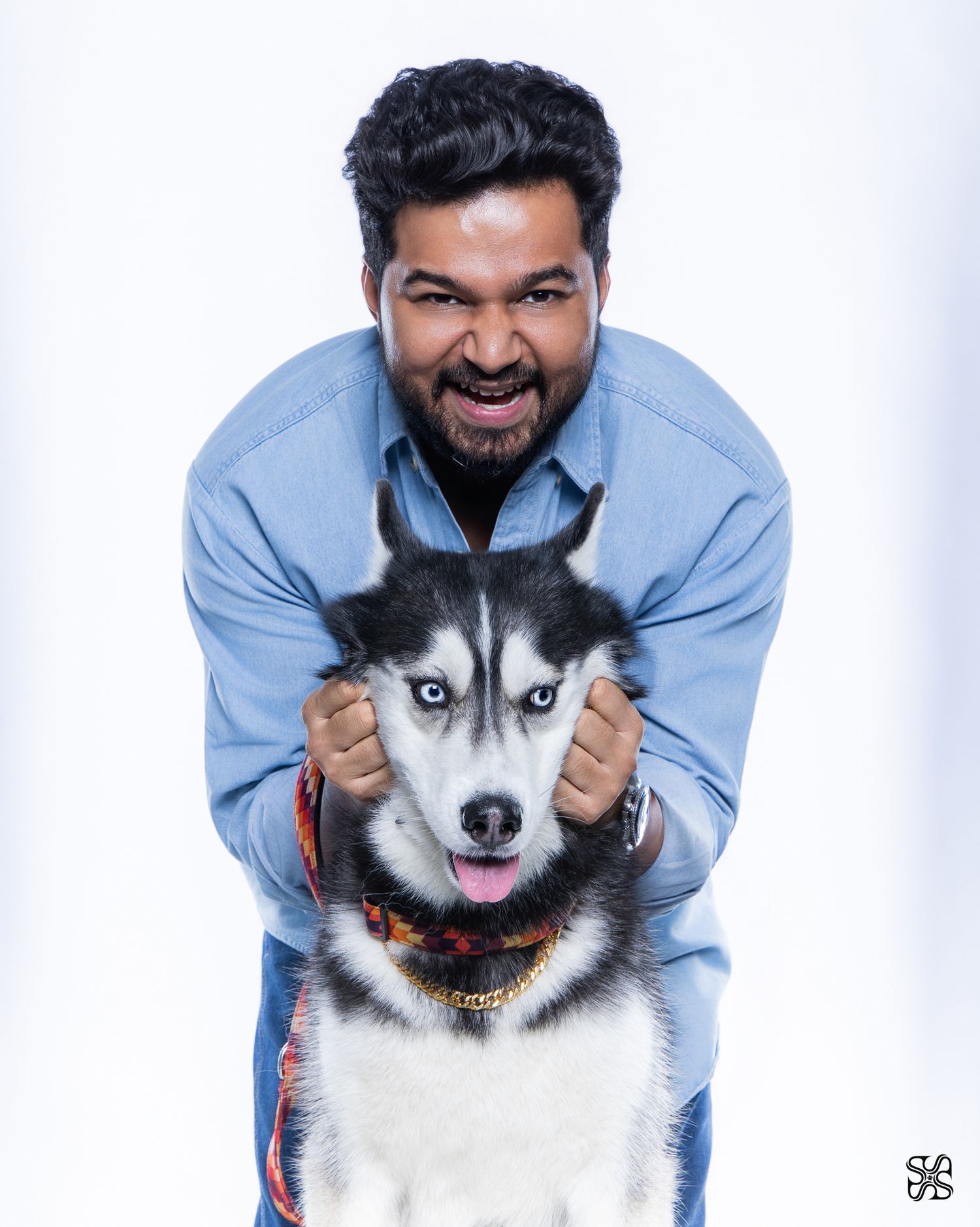 Smiling bearded man in blue shirt posing with a Siberian Husky dog against white background.