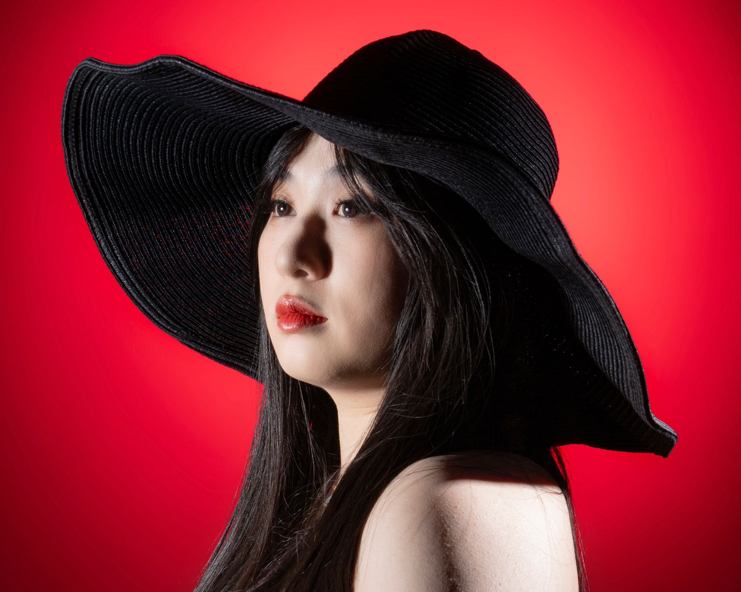 Fashion portraits with wide-brimmed black hat against vibrant red background.