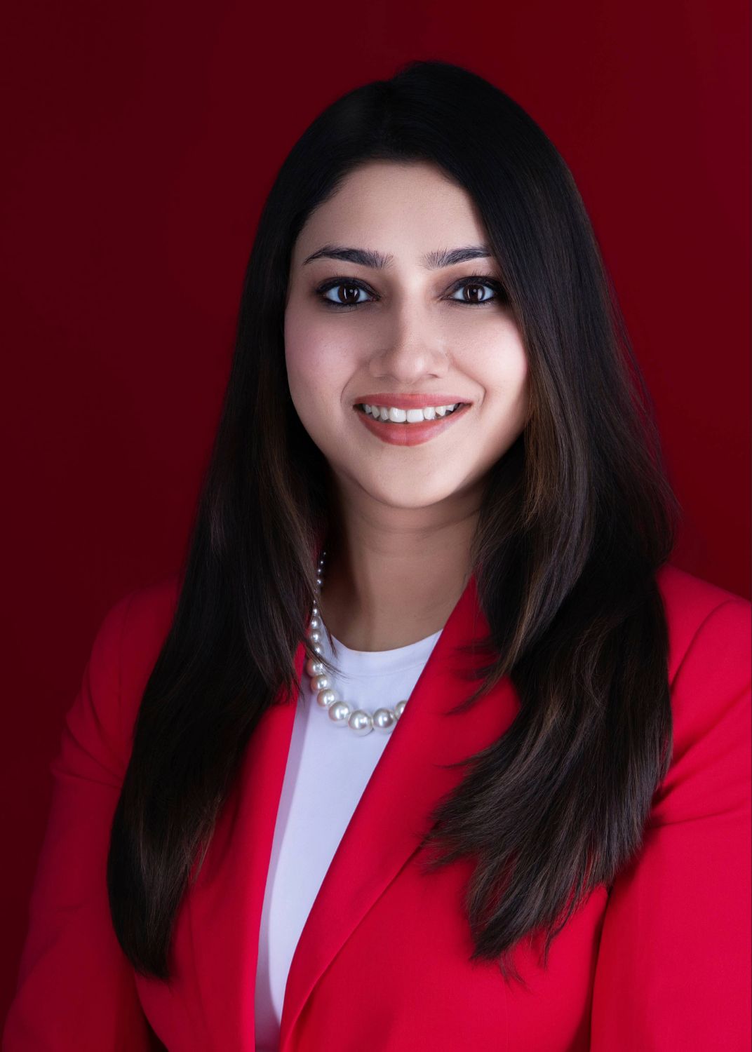 Professional studio portrait against deep red background featuring bright red blazer and white top.