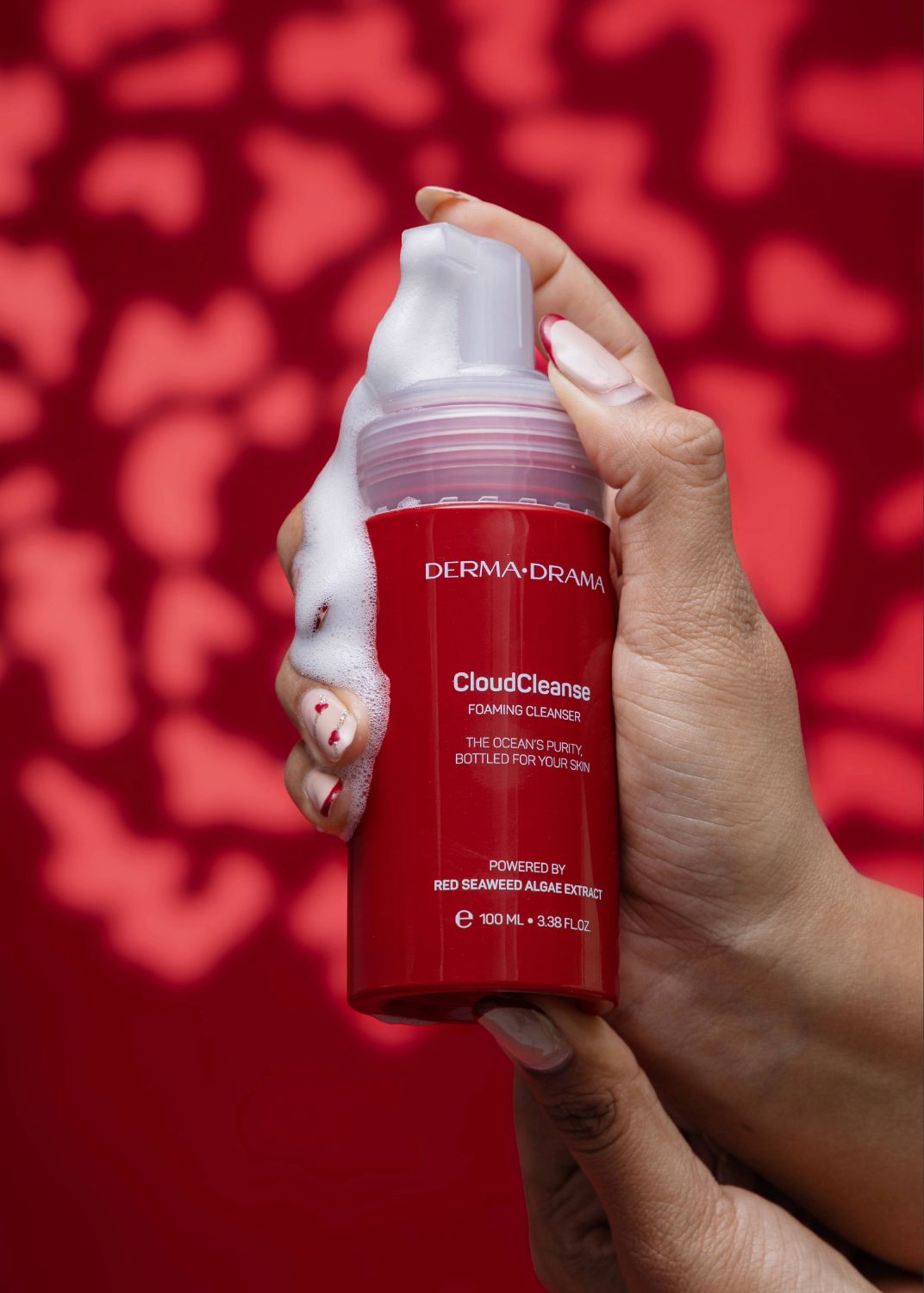 Hands hold a red skincare jar against a red background with heart-shaped bokeh lighting effects.