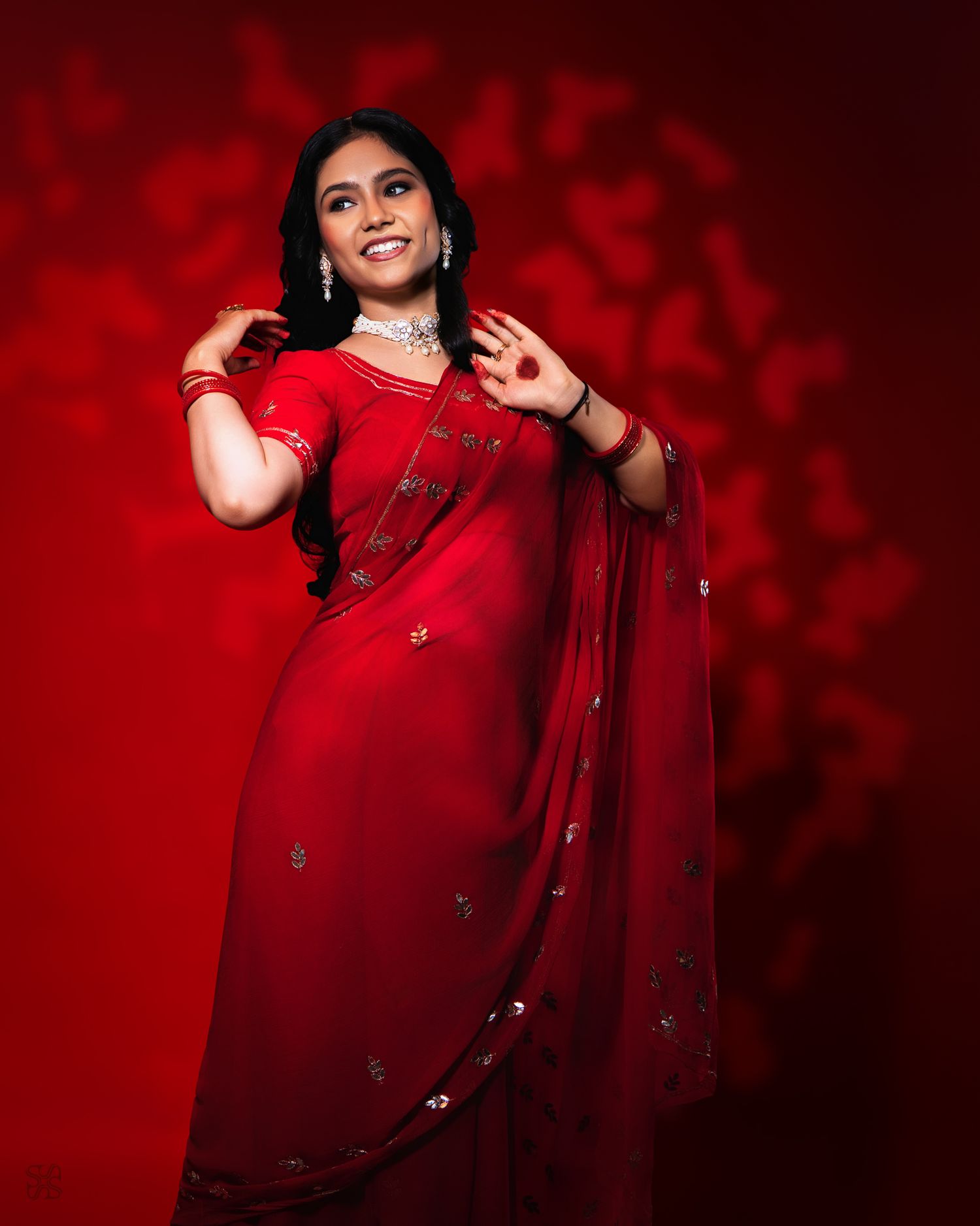 Woman in elegant red saree with silver jewelry posing gracefully against a red background.