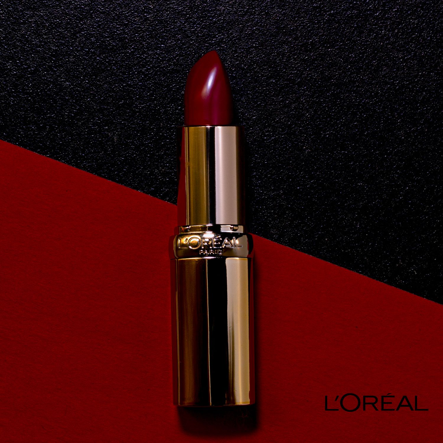 A L'Oreal lipstick in metallic gold packaging shown from different angles against dark and red backgrounds.