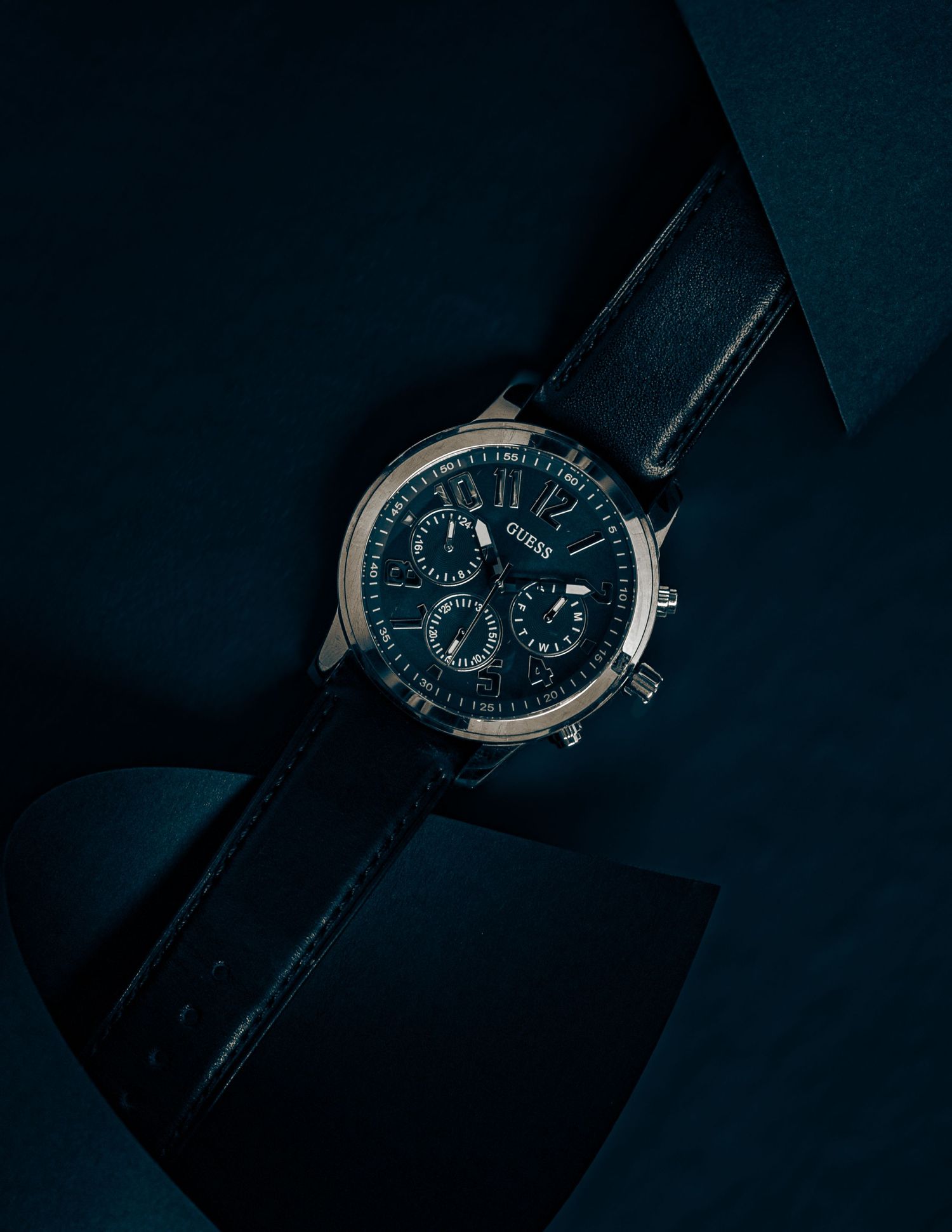 Luxury chronograph watch with blue dial photographed in dramatic low-key lighting against dark background.