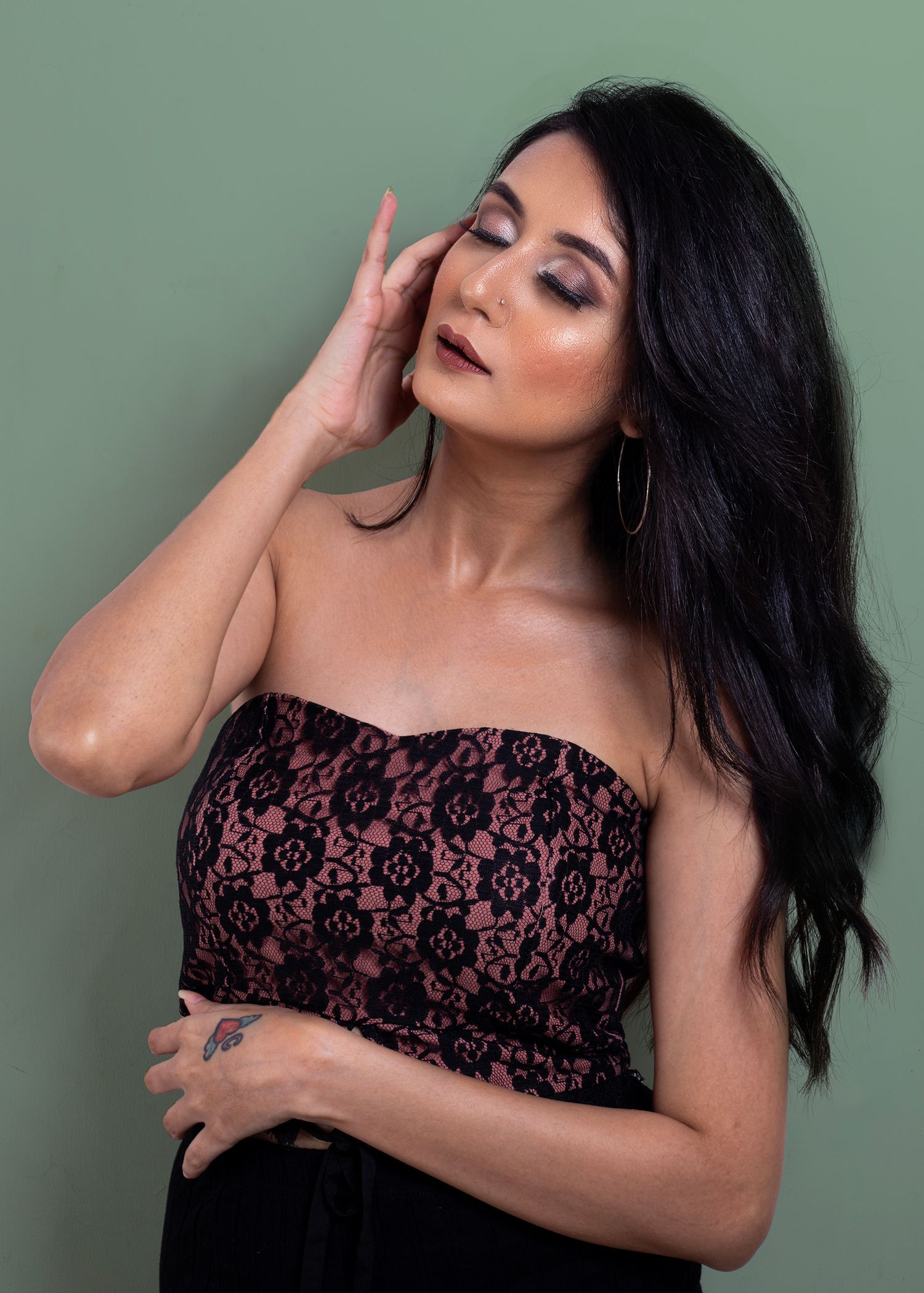 Fashion model poses in burgundy lace top against sage green background.