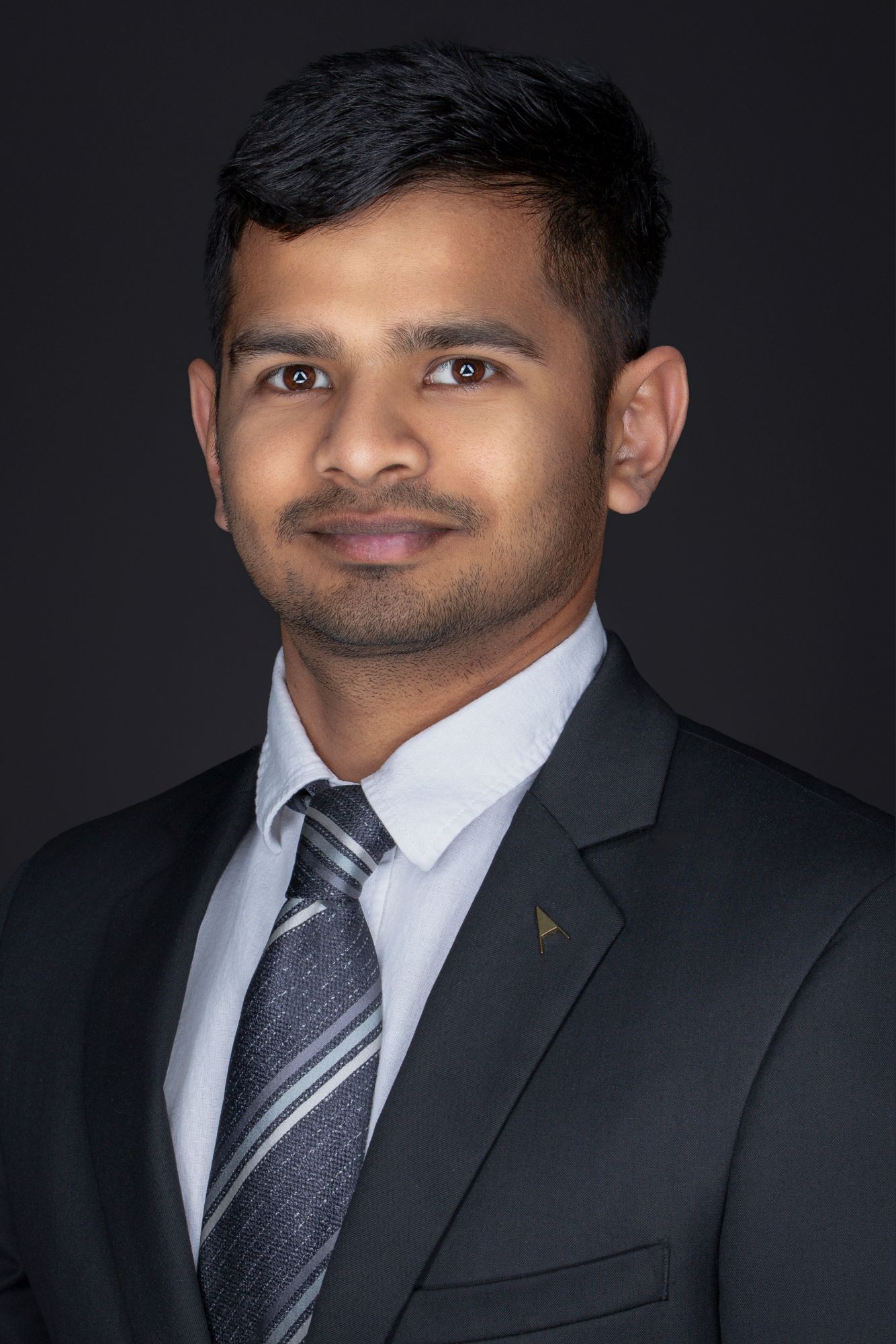 Professional portrait of person wearing dark suit and striped tie against black backdrop.