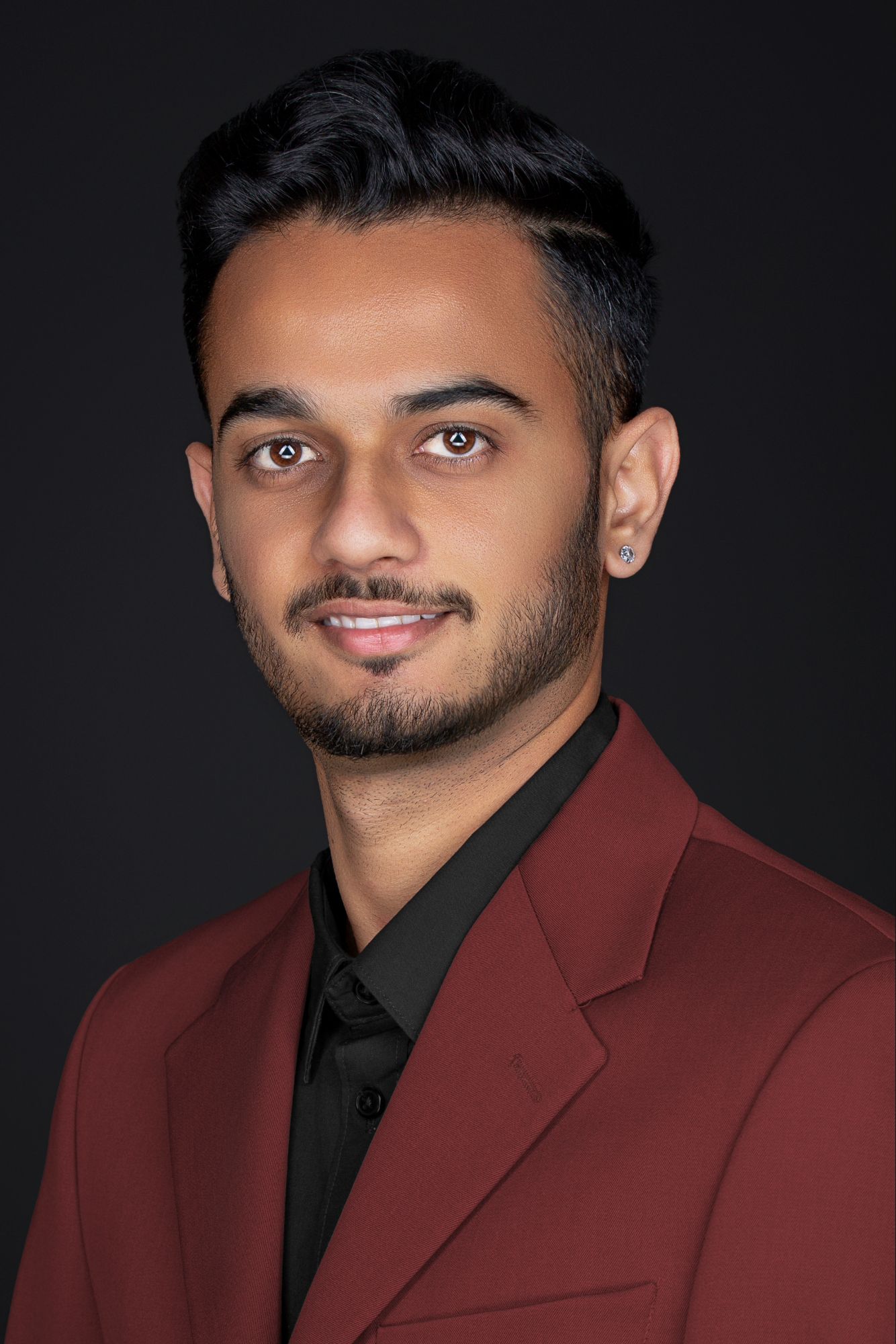 Professional headshot portrait of someone wearing a burgundy blazer and black shirt against dark background.