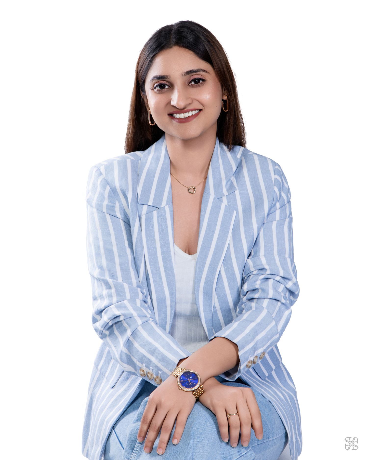 A smiling young woman in a light blue striped blazer and jeans, wearing a blue watch, posed against a white background.