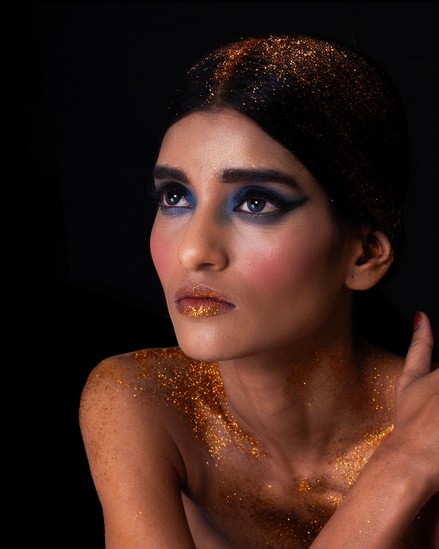 Creative beauty portrait with gold glitter makeup and dark dramatic lighting.
