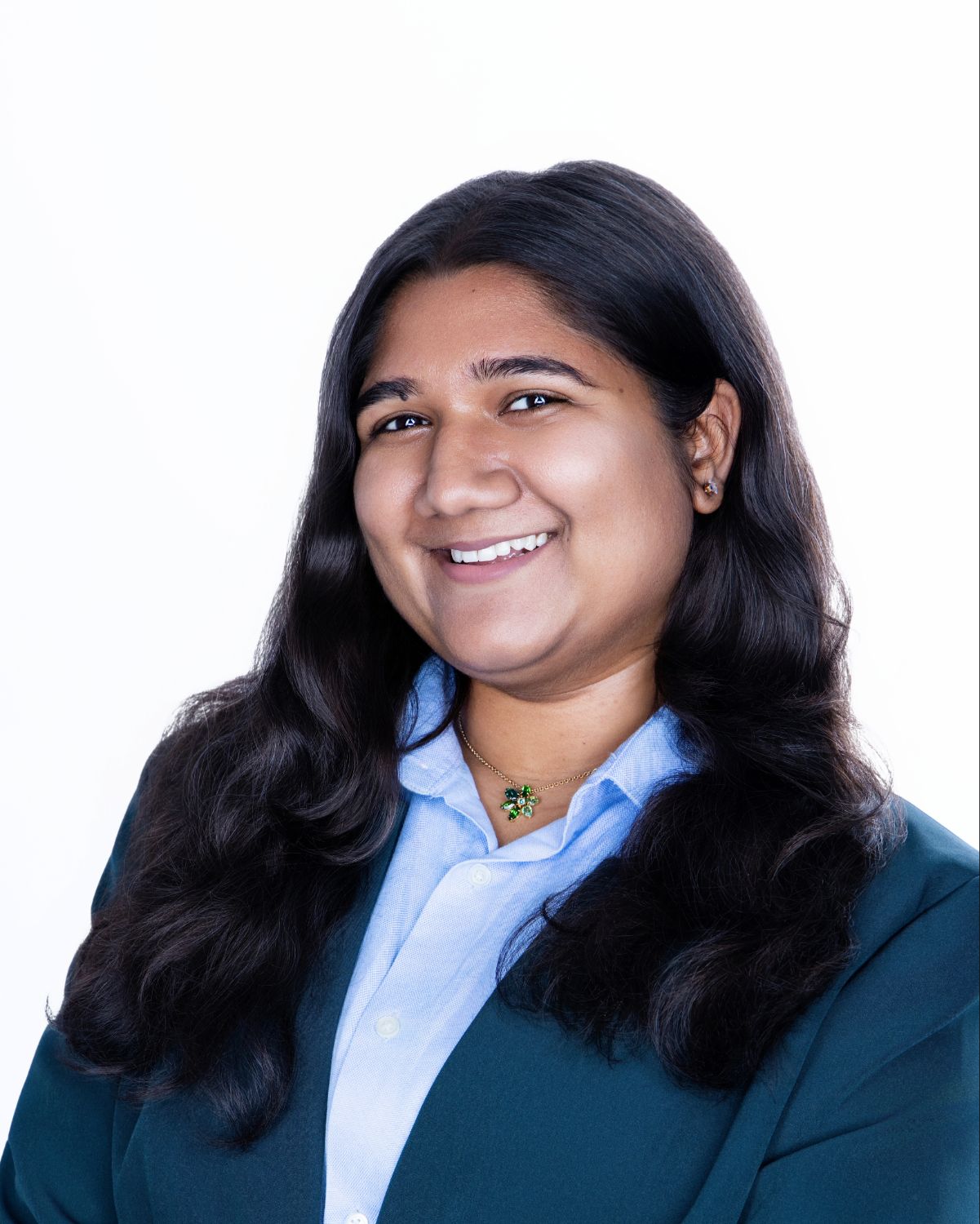 Professional headshot of a smiling woman with wavy black hair wearing a teal blazer and light blue shirt.