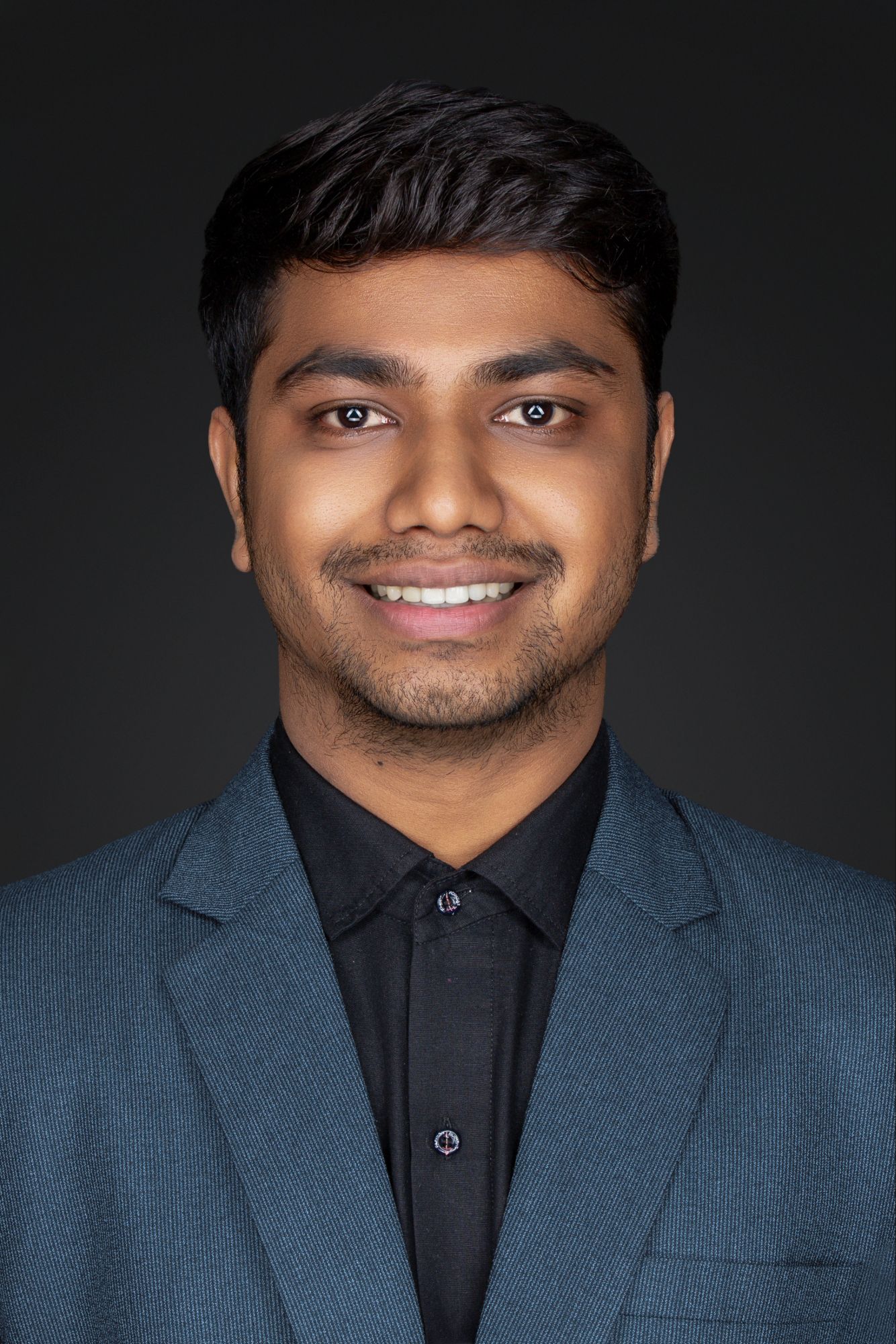 Professional headshot of someone wearing a blue blazer and black shirt against a dark background.