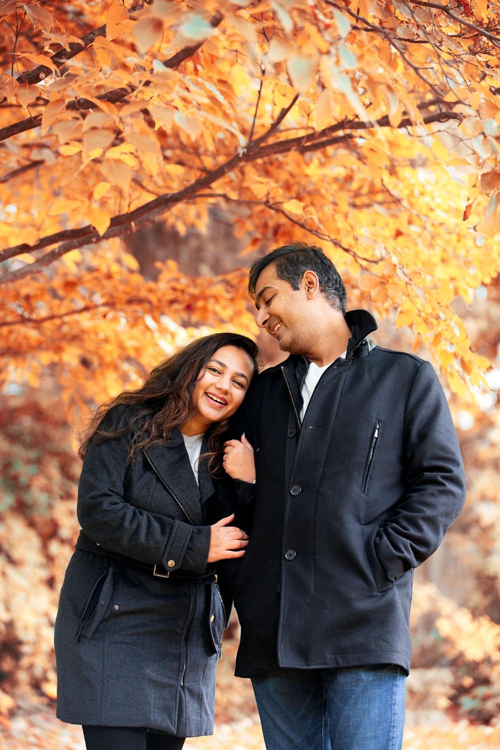 Couple laughing together under autumn trees with golden orange leaves.
