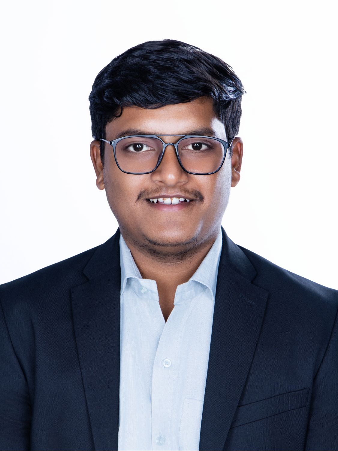 Young professional man in black blazer and glasses smiling confidently against white background.