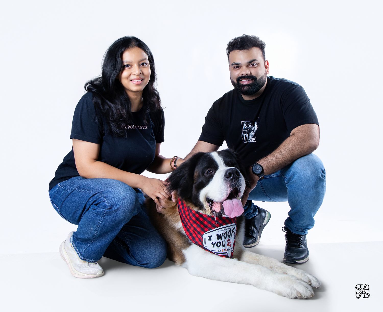 A couple in black t-shirts and jeans pose with a large Saint Bernard dog wearing an 'I Want You' bandana.