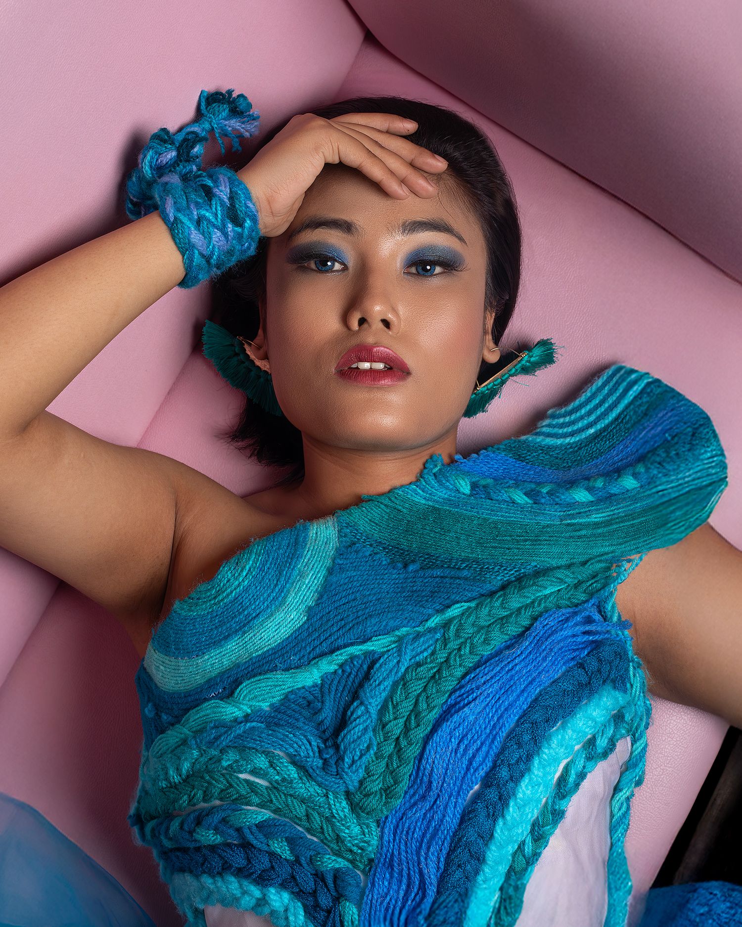 Fashion portrait with vibrant blue silk scarf and dramatic makeup against pink backdrop.