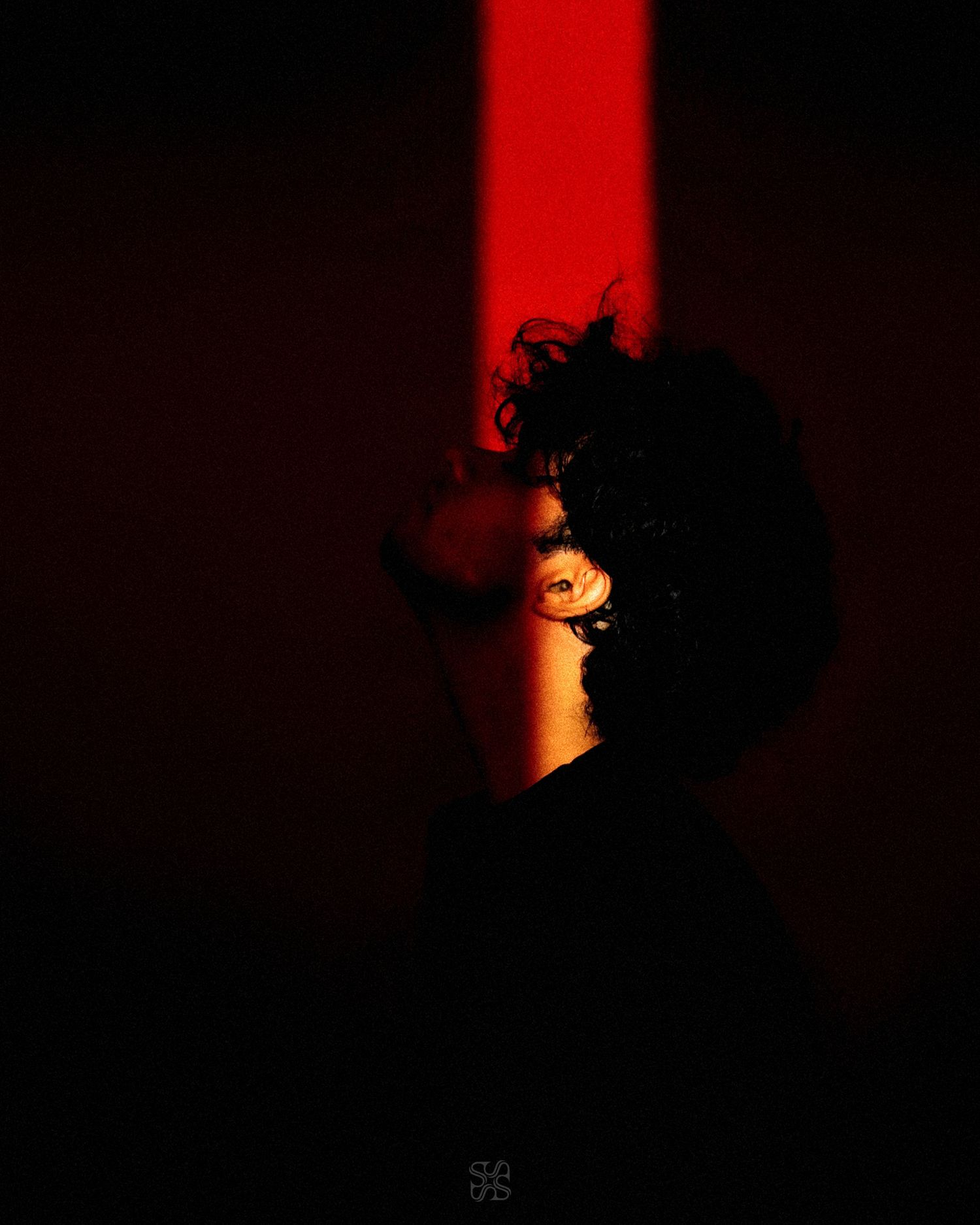 Person with curly hair illuminated by a dramatic red light beam against a dark background.