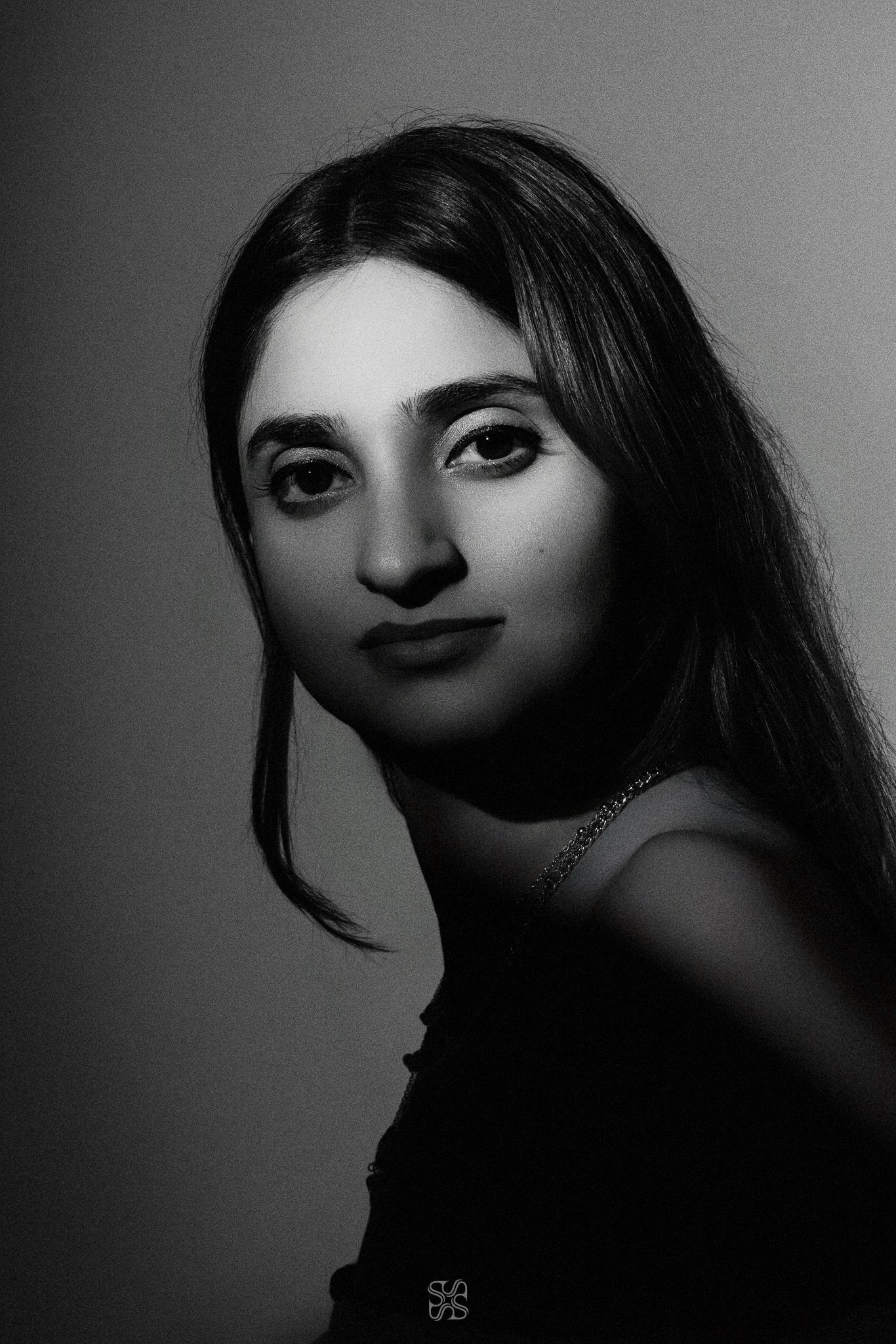 Black and white portrait of a young woman with long dark hair wearing a necklace, gazing softly at the camera.