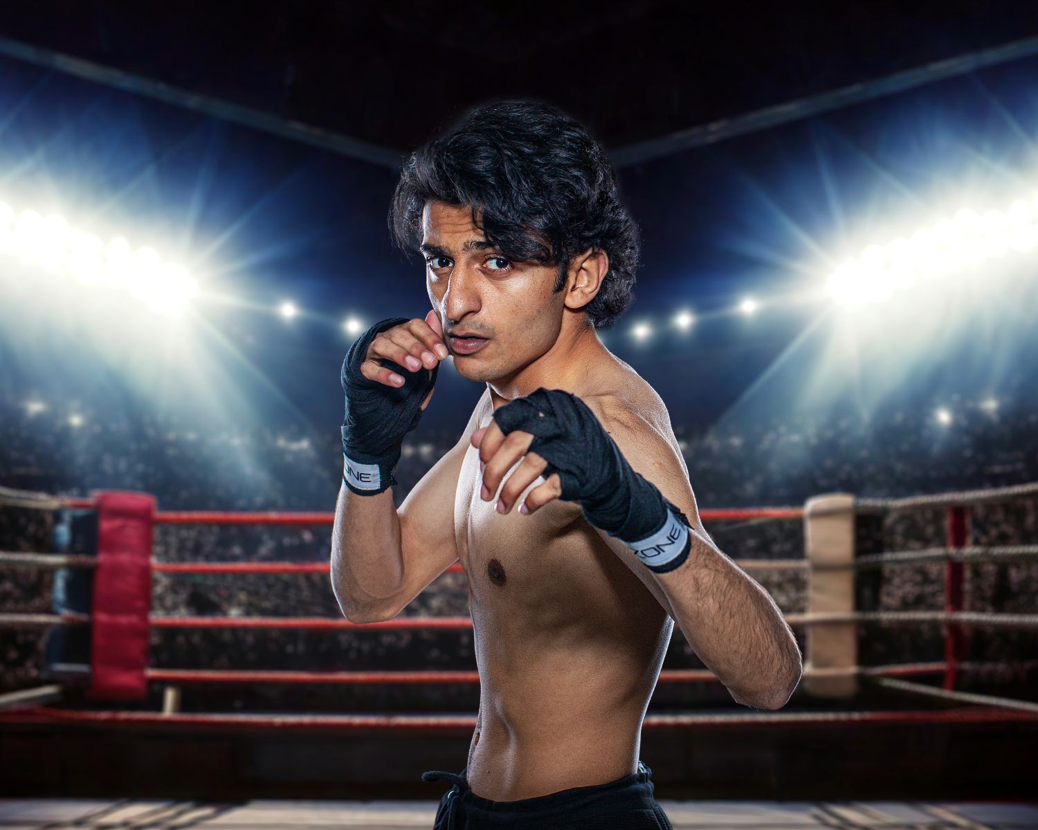 Young male MMA fighter in boxing stance inside a professional ring under bright stadium lights.