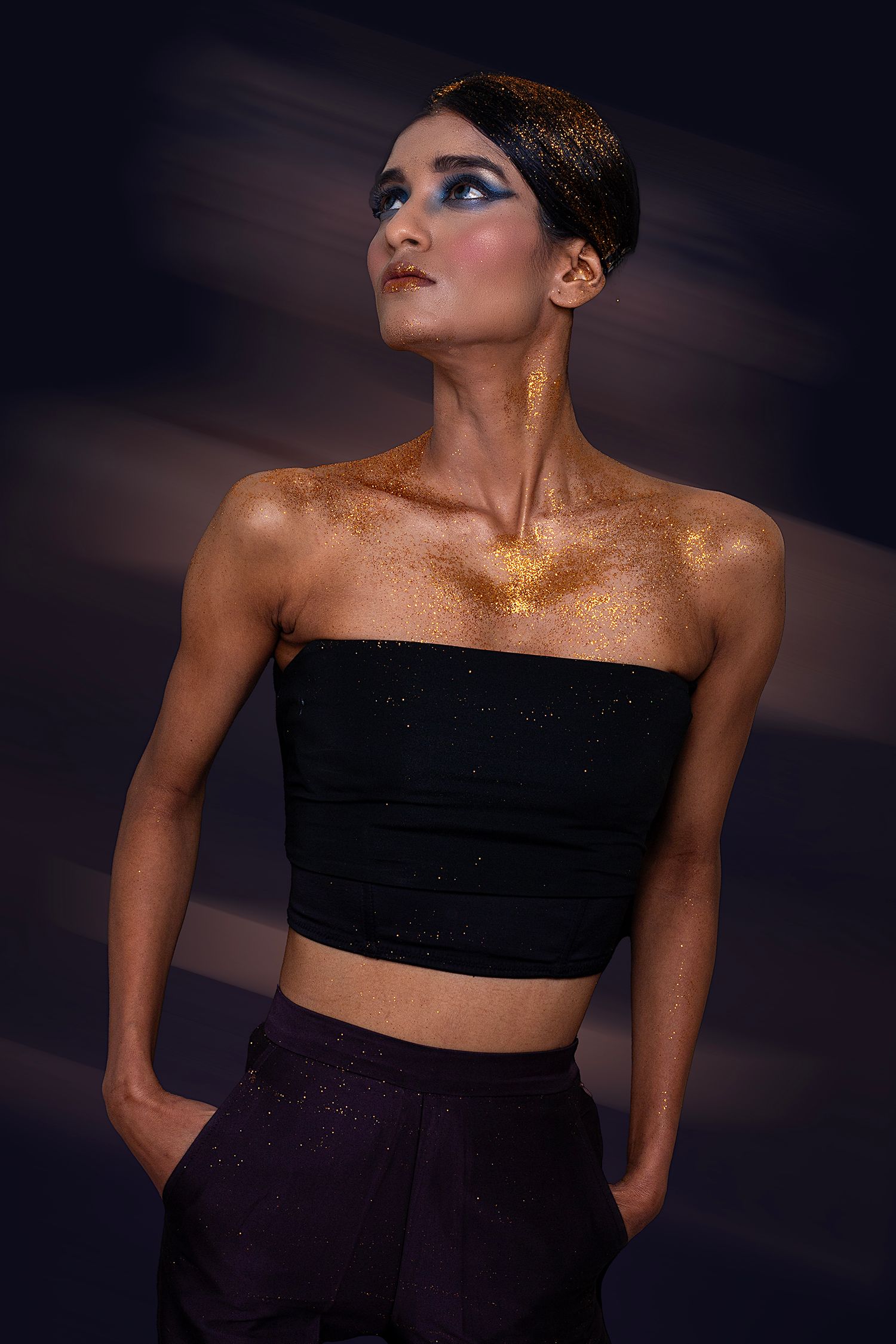 Dramatic portrait series with gold glitter makeup and black top against dark background.