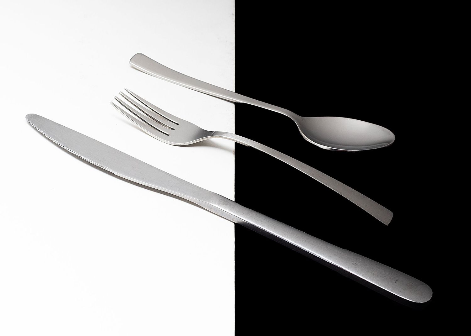 Dramatic black and white photo of shiny silverware utensils casting shadows on a dark background.