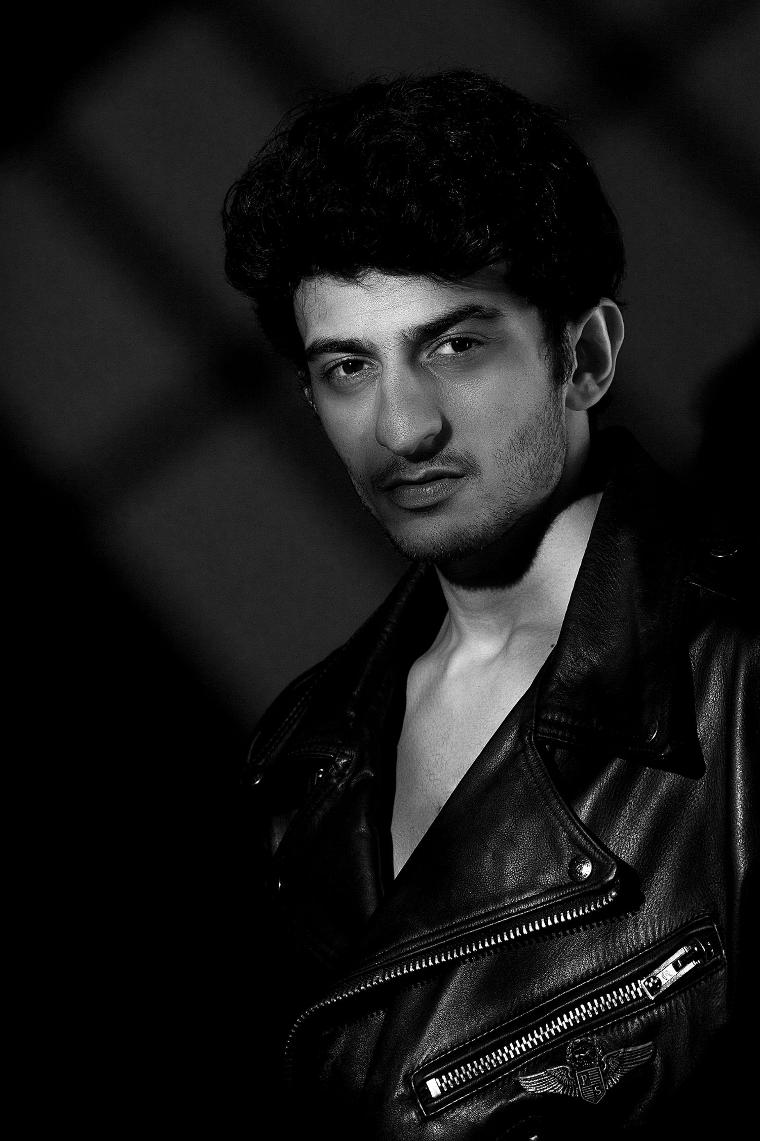 Dramatic black and white portrait in leather jacket with moody lighting and dark background.