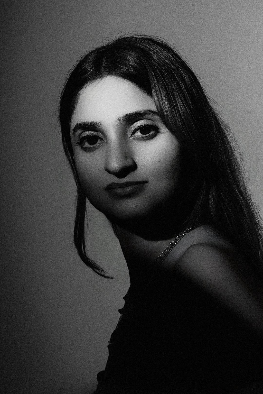 Black and white portrait of a young woman with long dark hair gazing softly at the camera against a neutral background.