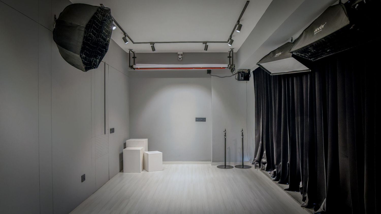Modern photography studio with softbox light, white walls, light wood floor, and black backdrop curtains.